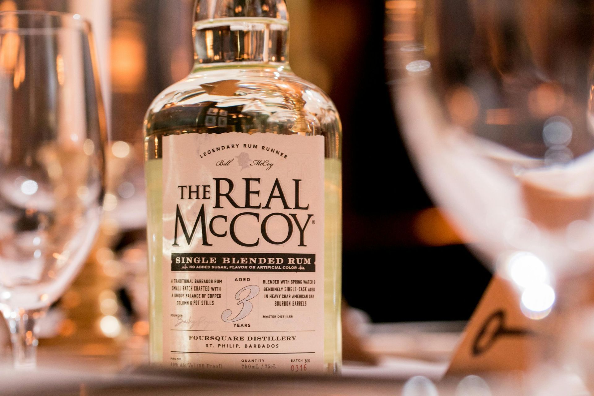 A bottle of the Real McCoy Rum is sitting on a table next to wine glasses.