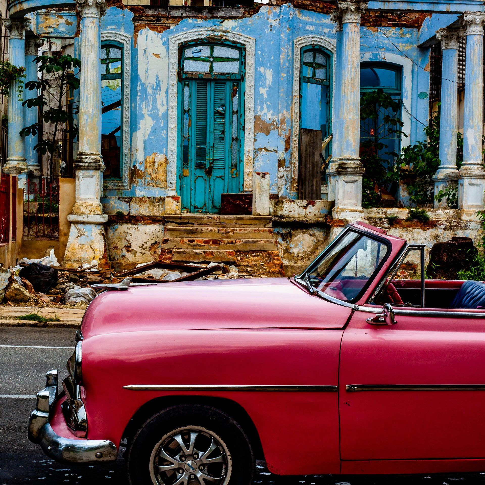 A pink car is parked in front of a blue building