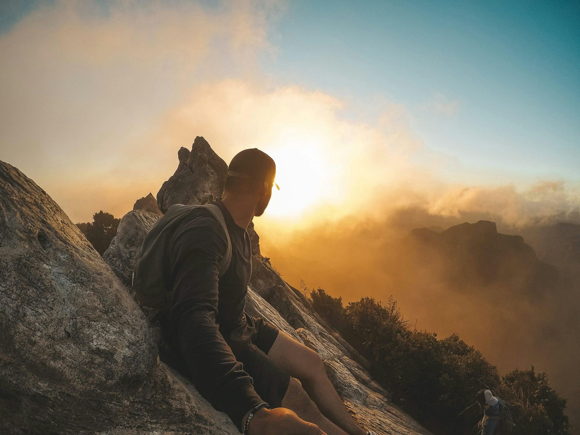 A man is sitting on a rock on top of a mountain at sunset.
