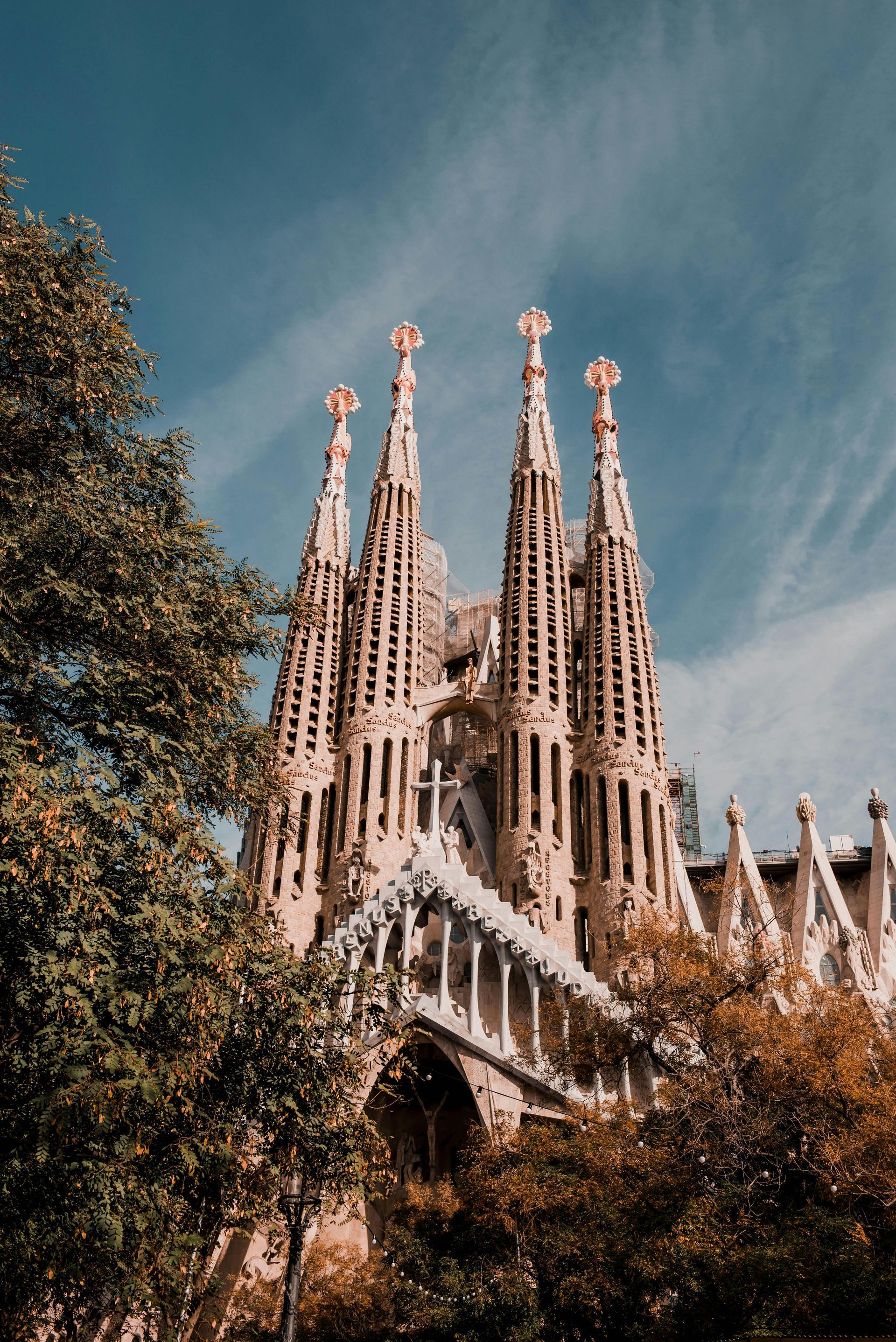 The Sagrada Familia Cathedral in Barcelona is surrounded by trees and a blue sky.