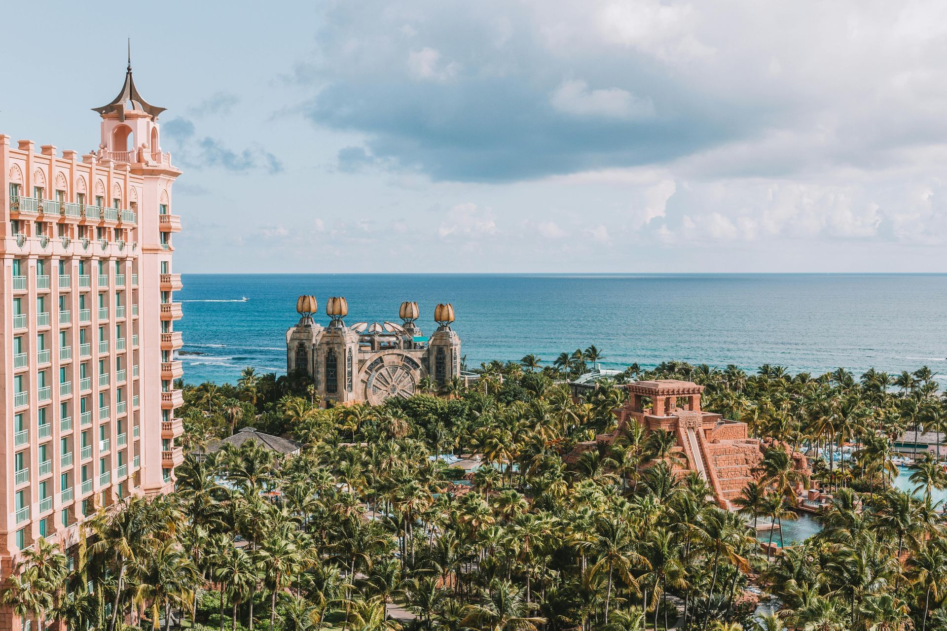 An aerial view of a large building surrounded by palm trees next to the ocean.