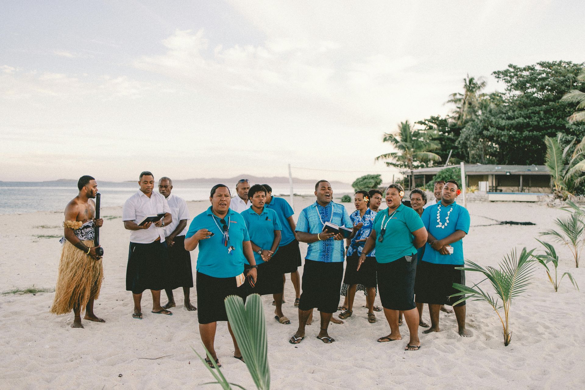 A group of people are standing on a beach doing a traditional Fiji dance.
