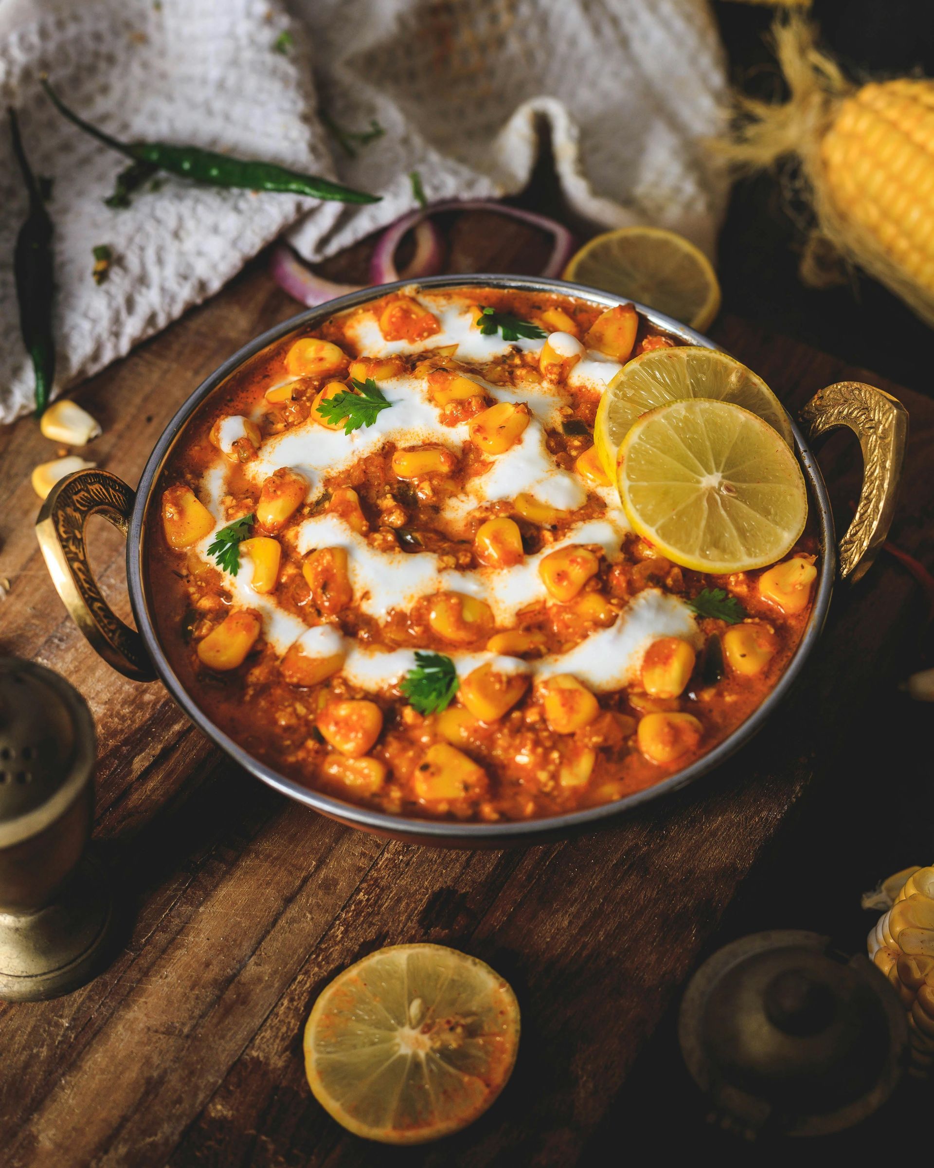 A bowl of Indian food with lemon slices on a wooden table.
