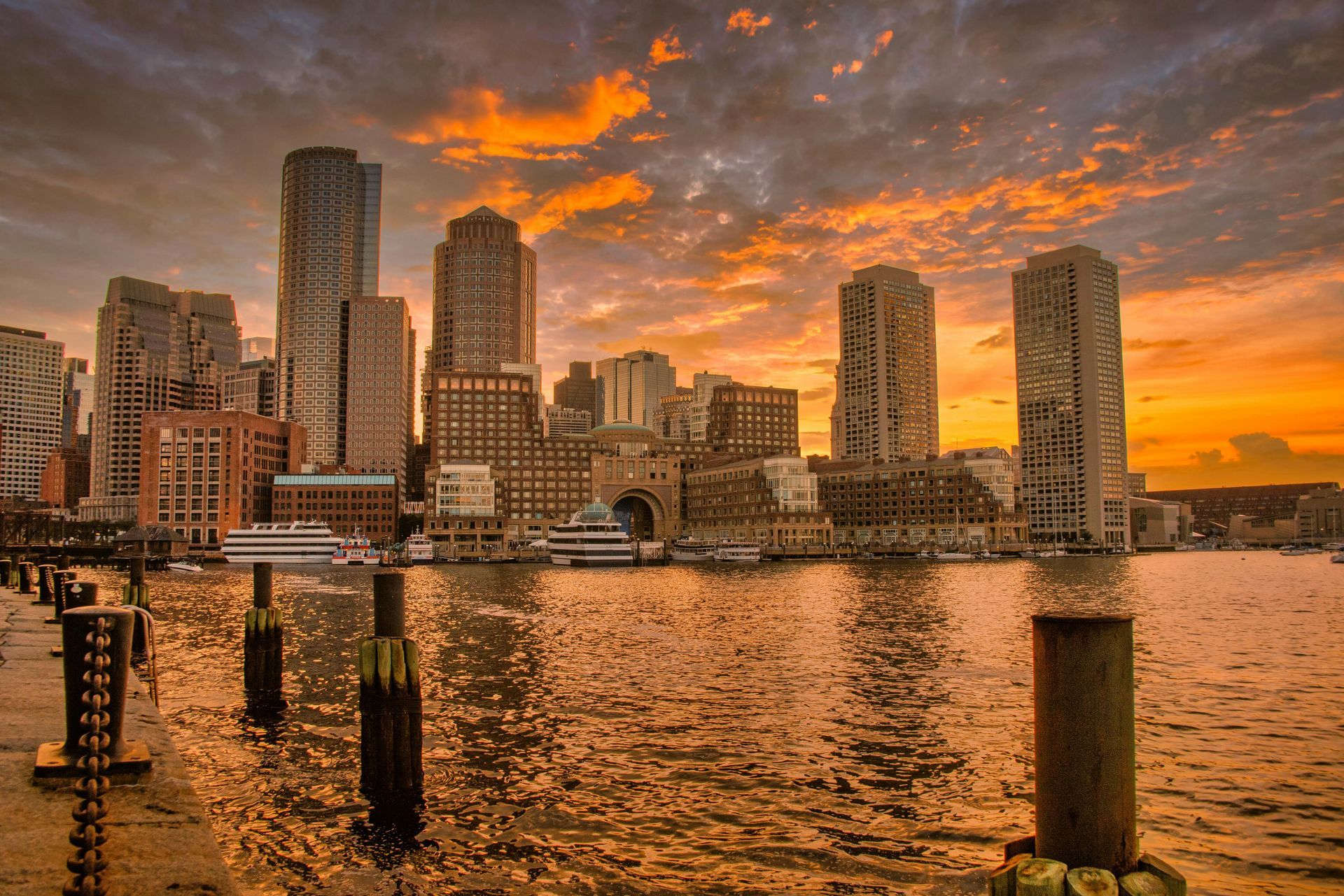 Boston city skyline is visible over a body of water at sunset.