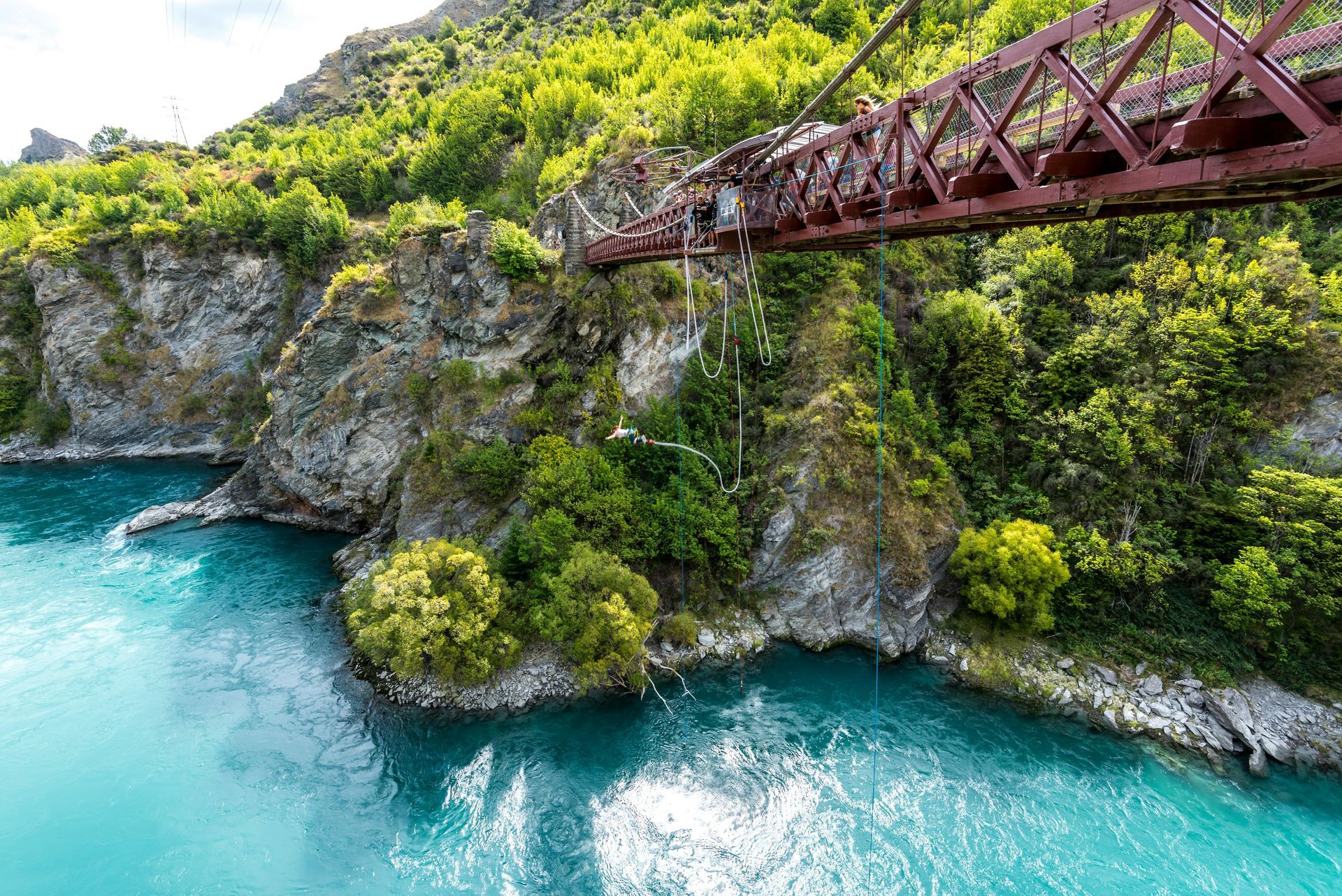 A person is jumping off a bridge over a body of water in Queenstown