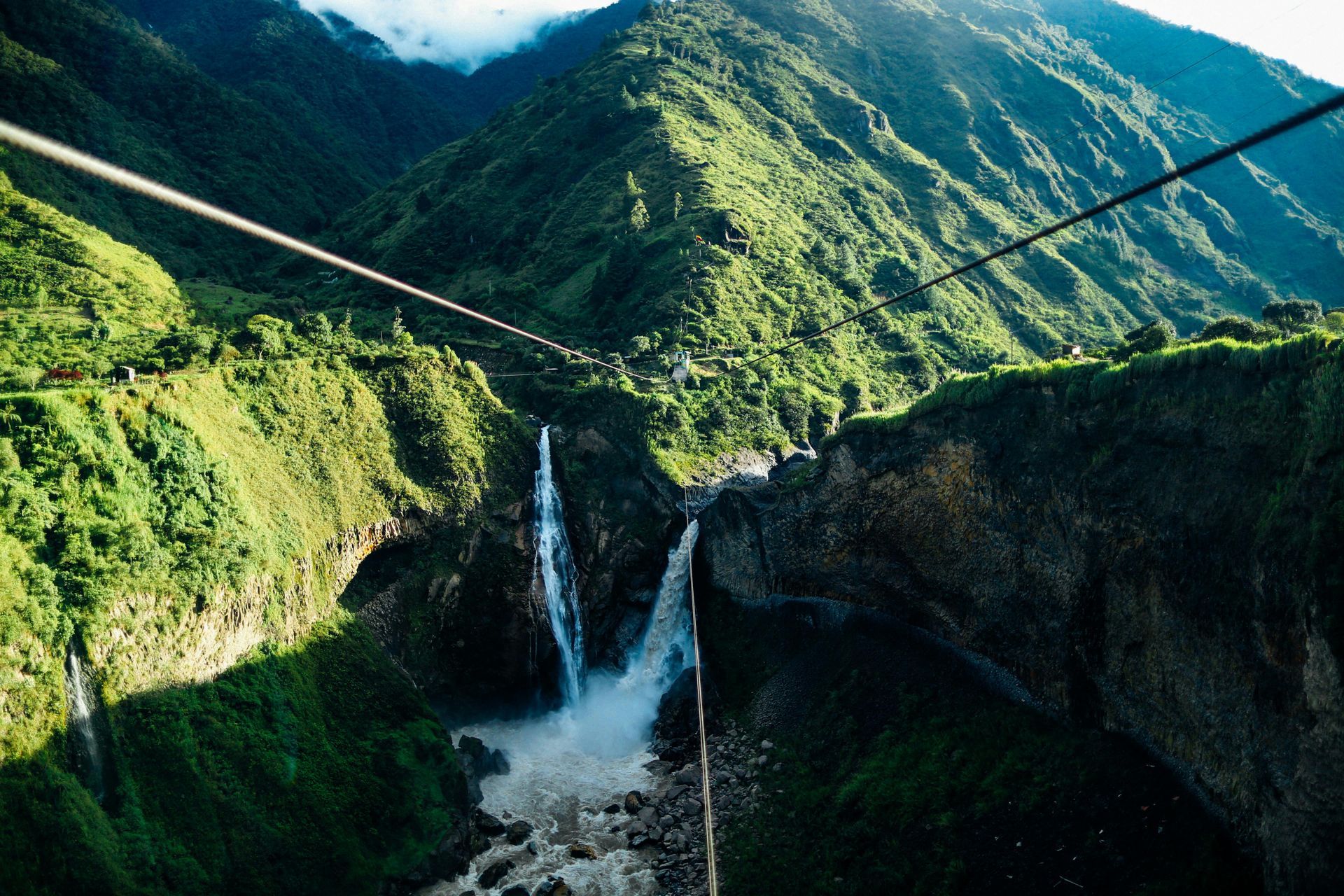 A person is riding a zip line over a waterfall in the mountains.