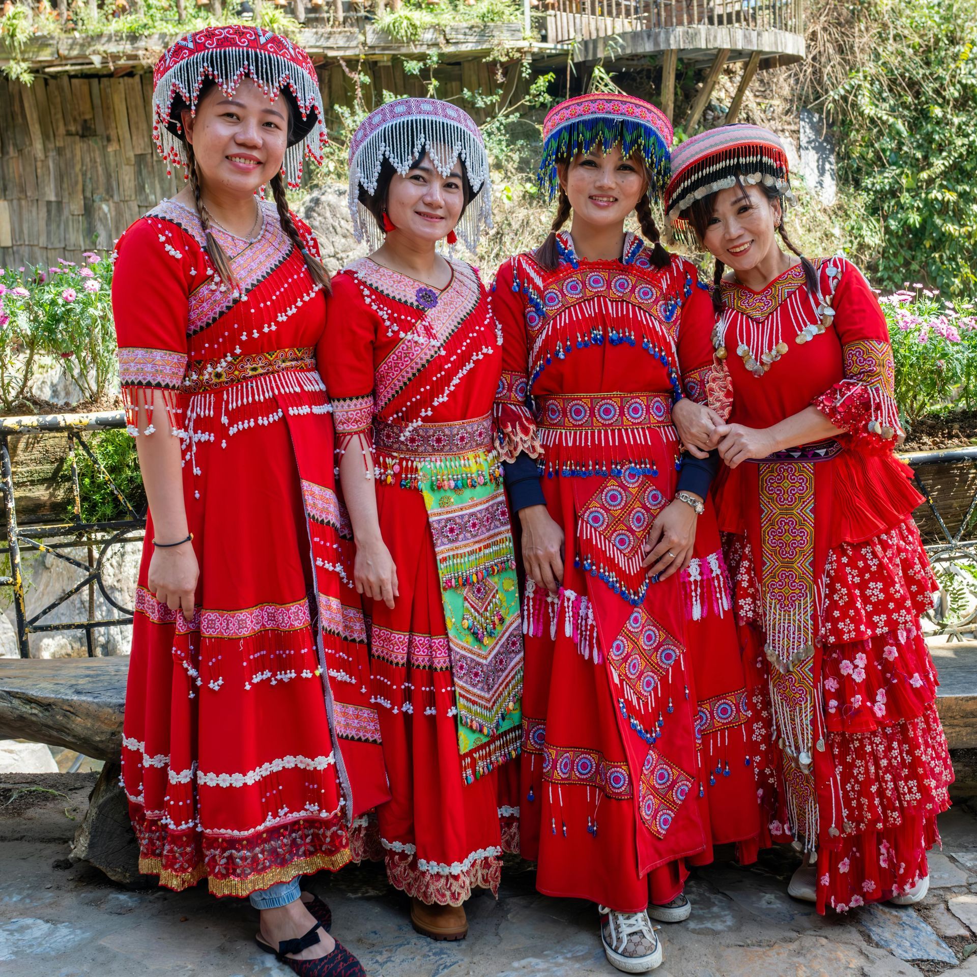 Four women wearing red dresses and hats pose for a picture in Hmong culture