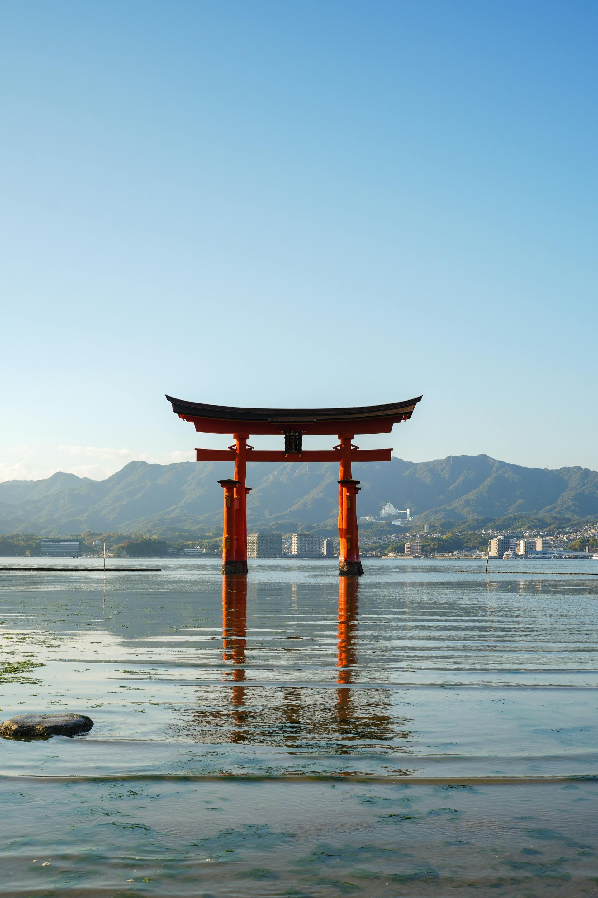 A red torii gate is in the middle of a body of water in Hiroshima