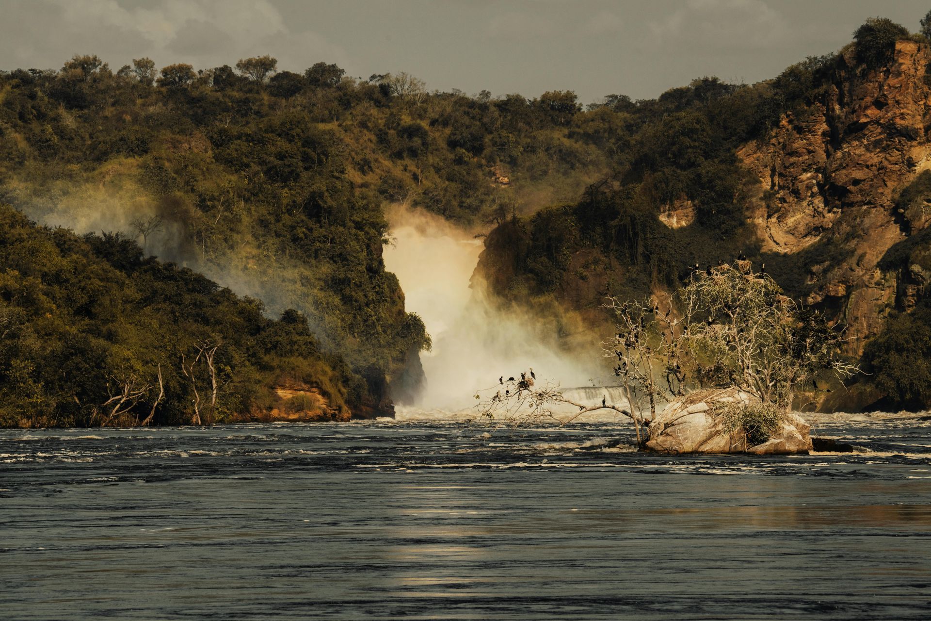 Murchinson Falls in the middle of a river surrounded by trees in Uganda