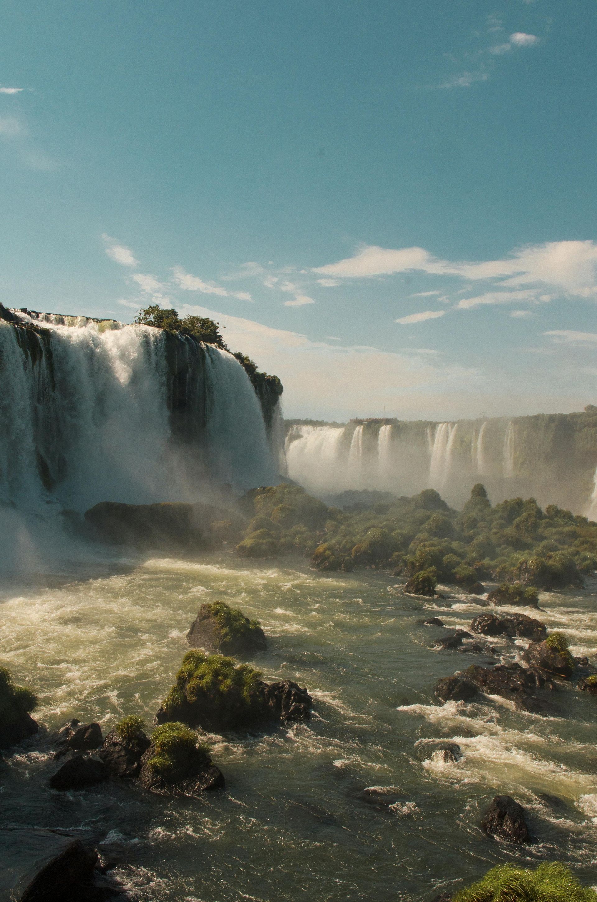 Iguazu Falls is surrounded by rocks and trees on a sunny day