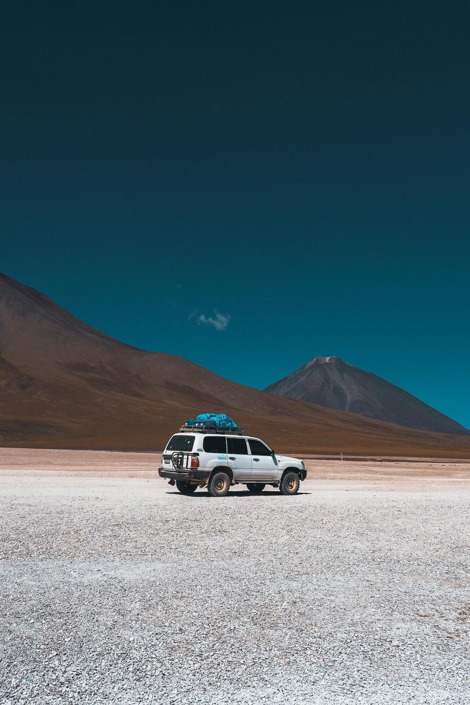 A white suv with a roof rack is parked in the middle of a salt flat.
