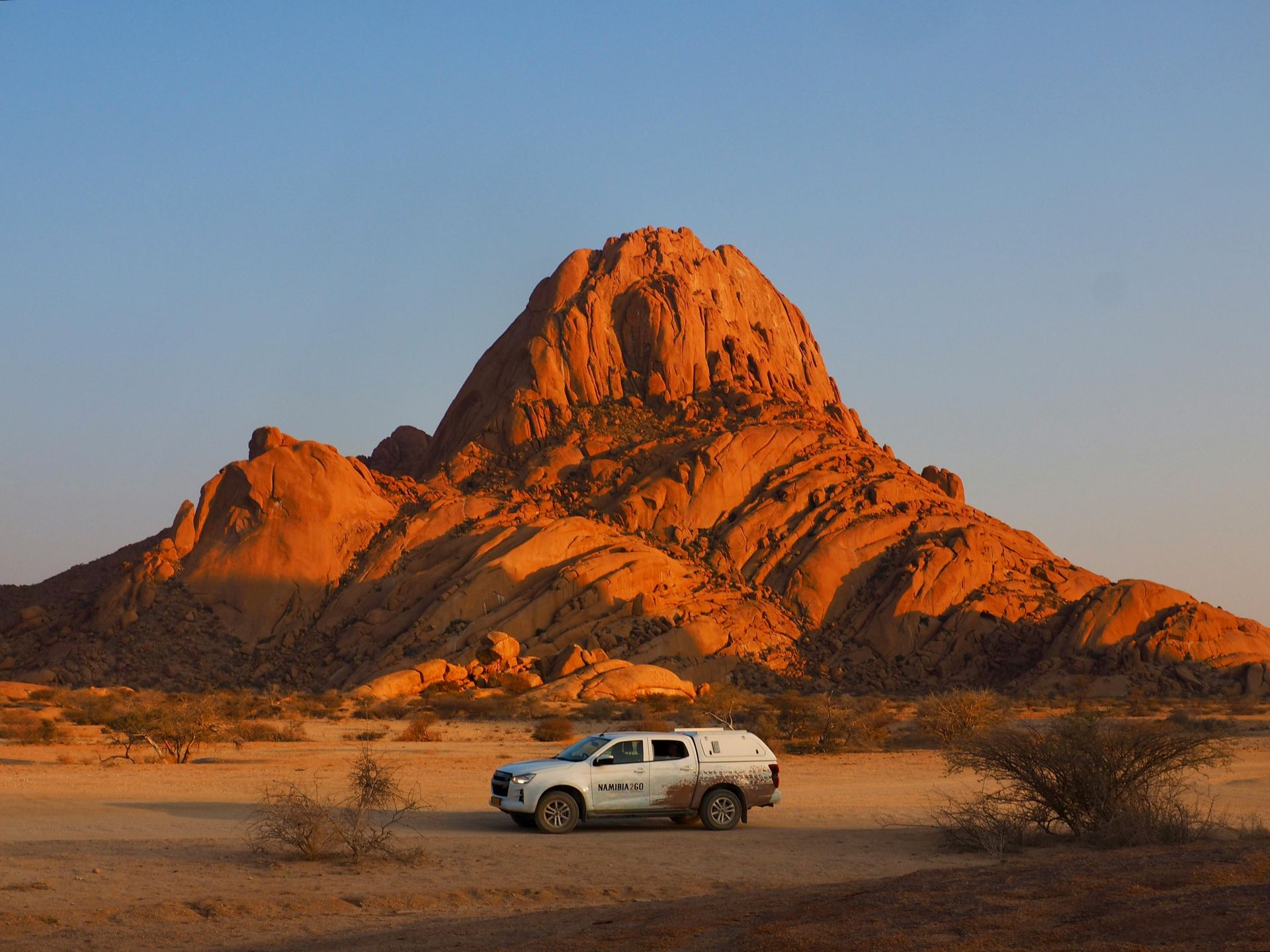 A 4x4 car is parked in front of a mountain in the desert in Namibia