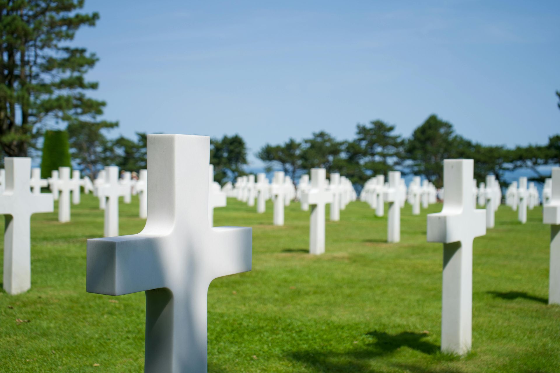 White crosses mark graves in a green field under a clear blue sky; a military cemetery.