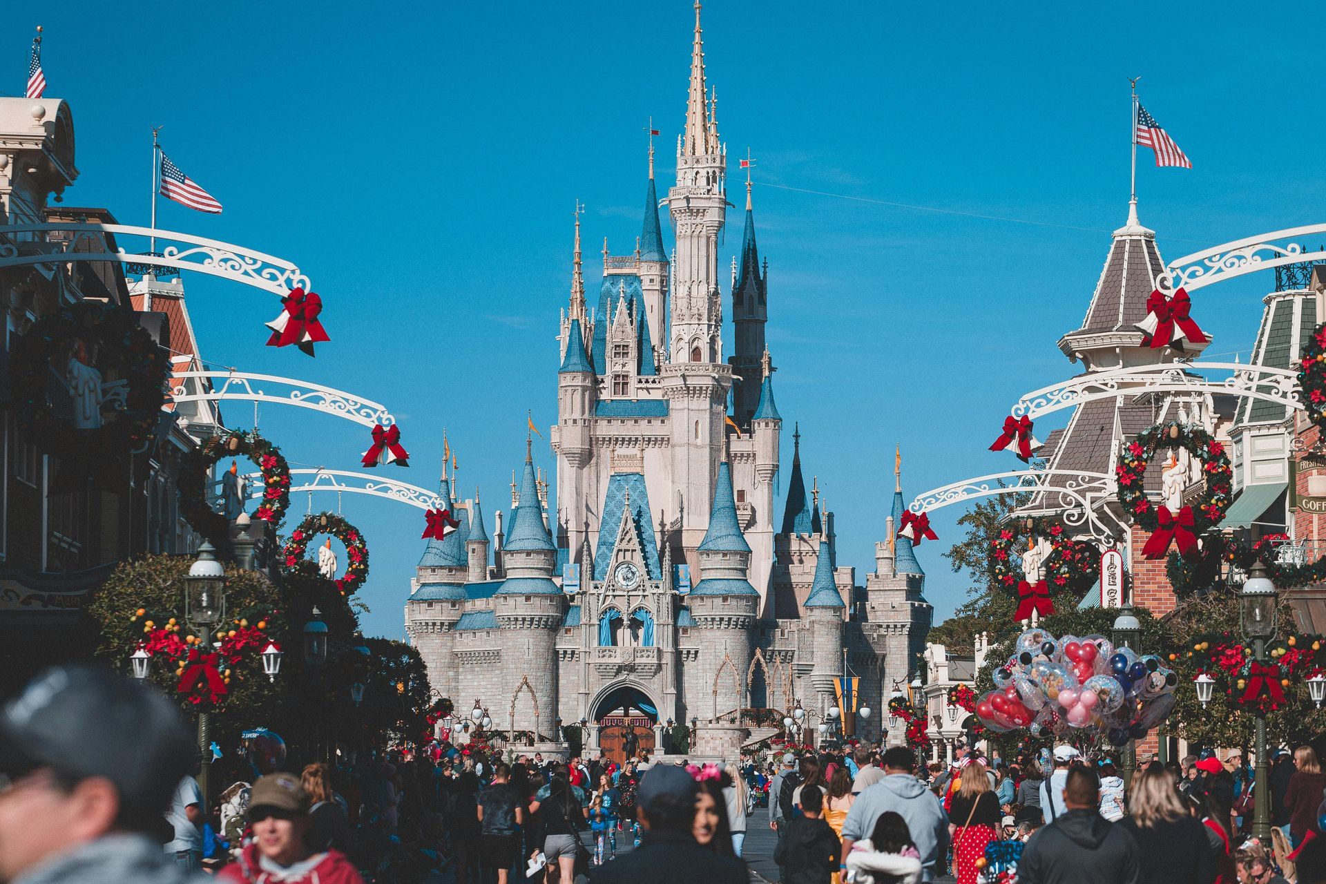 A crowd of people are walking in front of the castle at disney world.