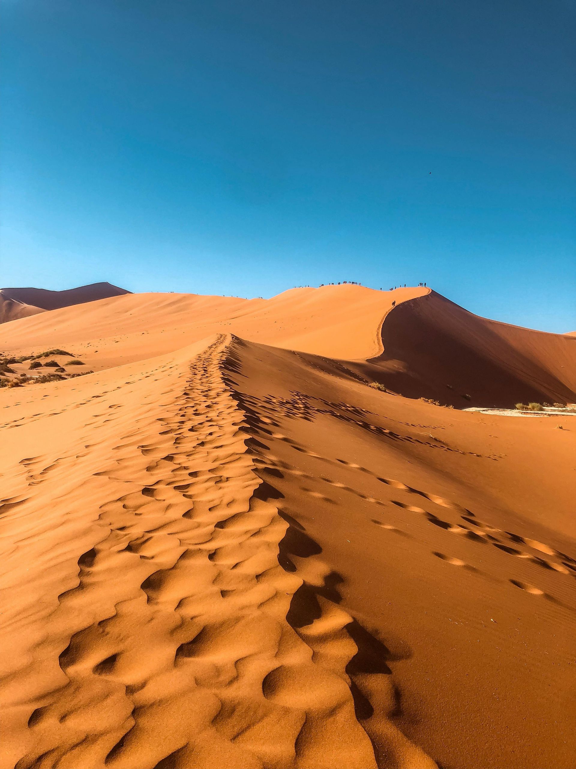 A person is walking up a sand dune in the desert.