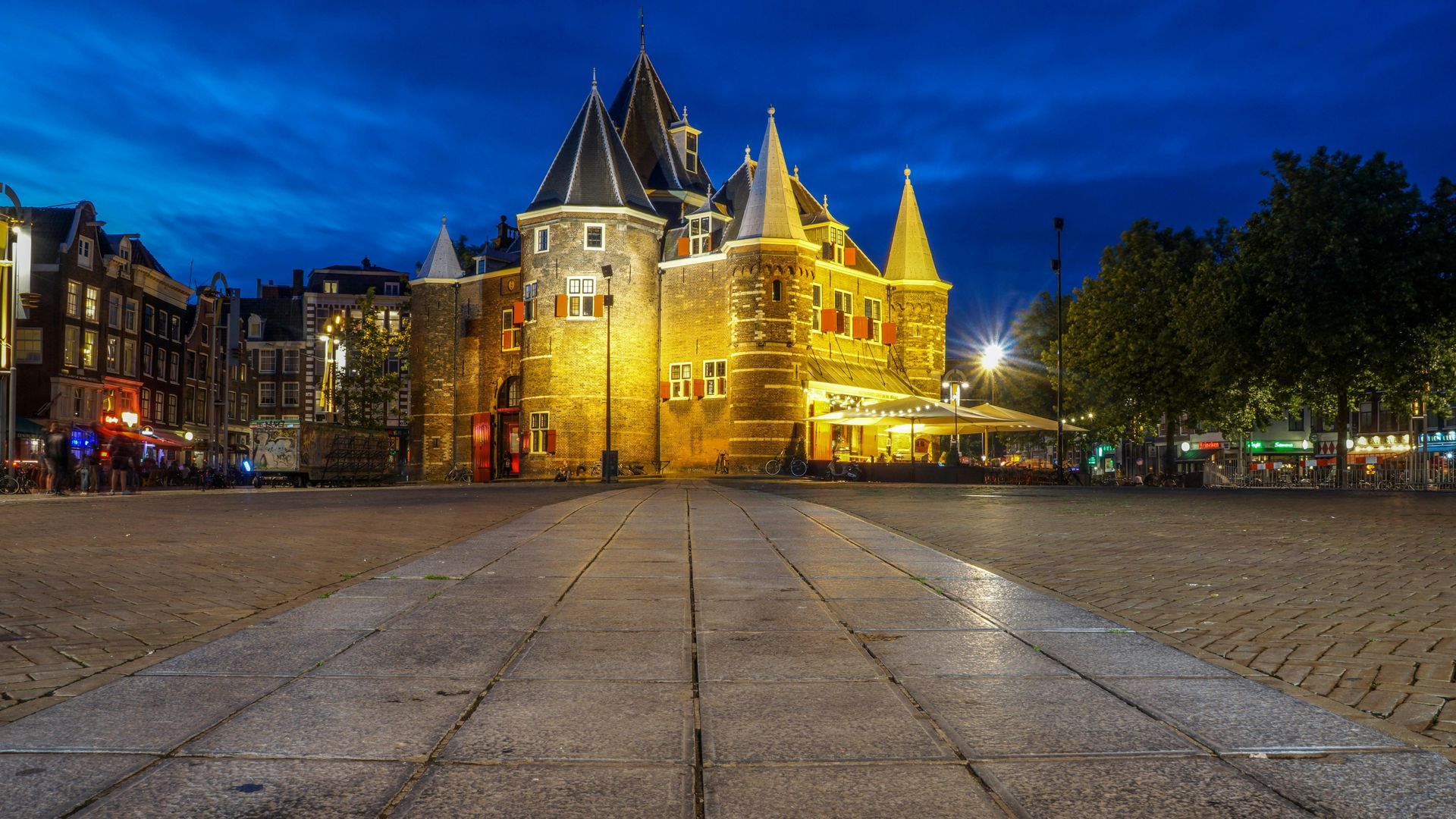 A large building with a castle in the background is lit up at night.