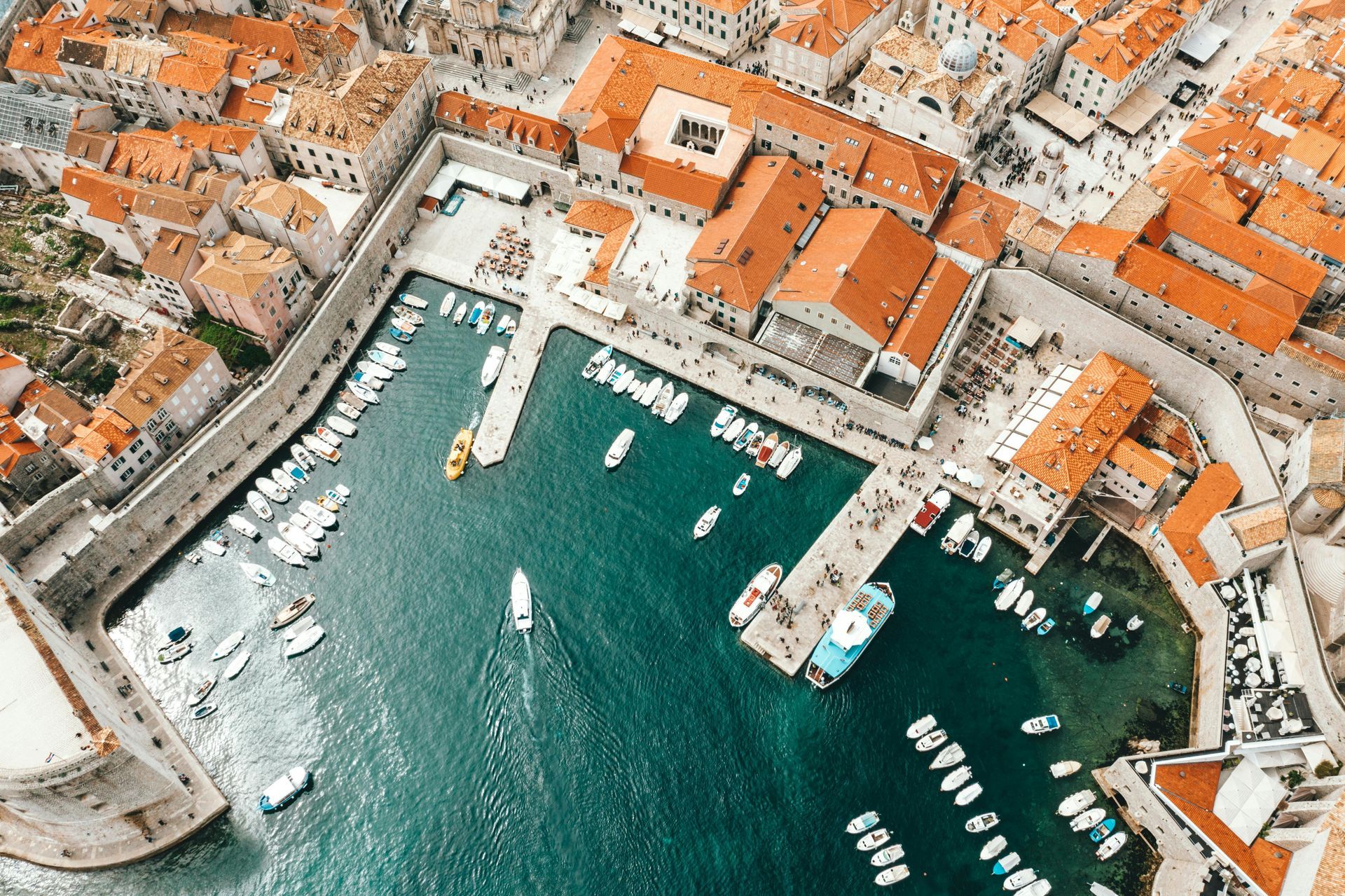An aerial view of Dubrovnik harbour with boats docked and the walled city in the background.