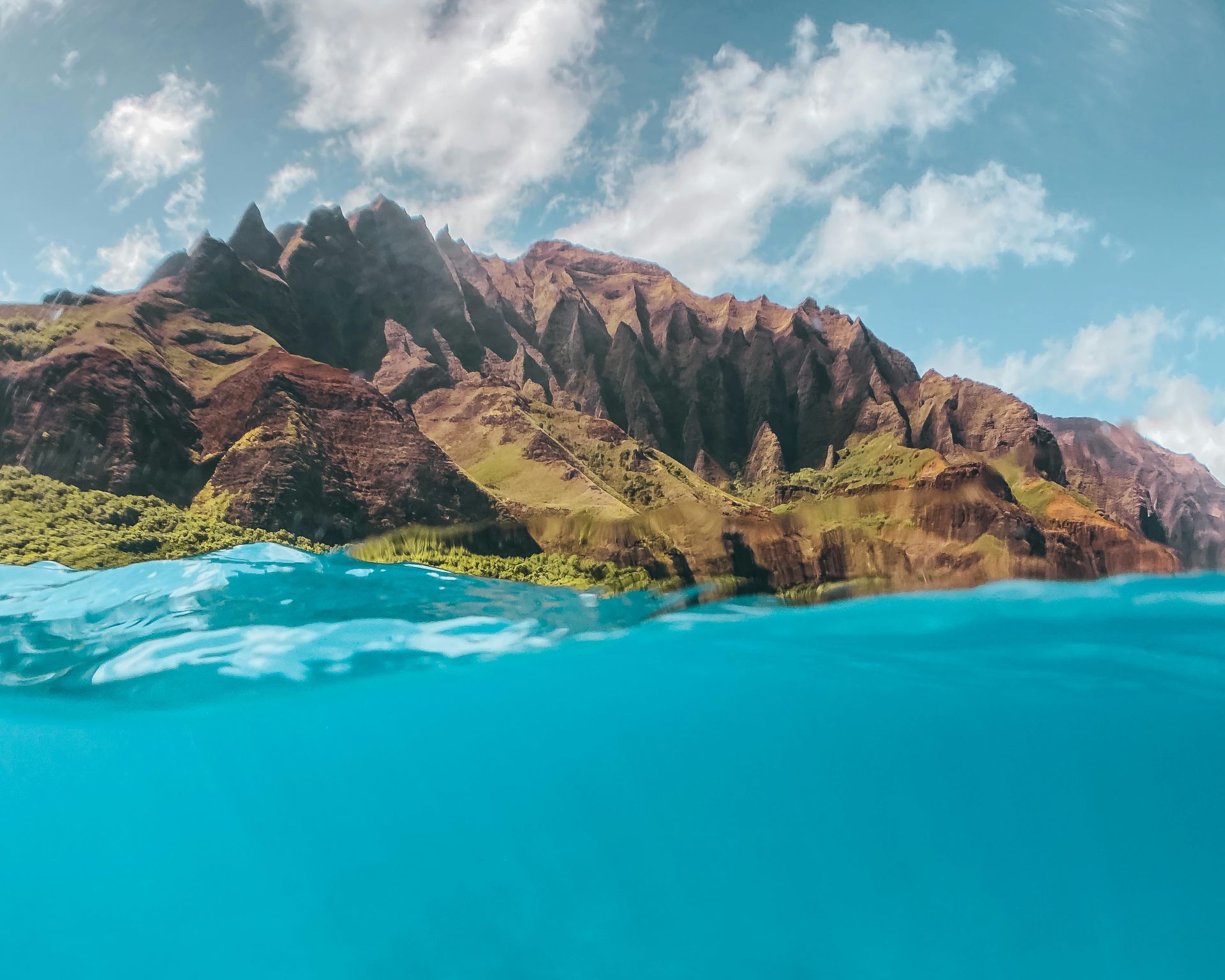 A half underwater view of a mountain surrounded by water of Na Pali Coast Hawaii