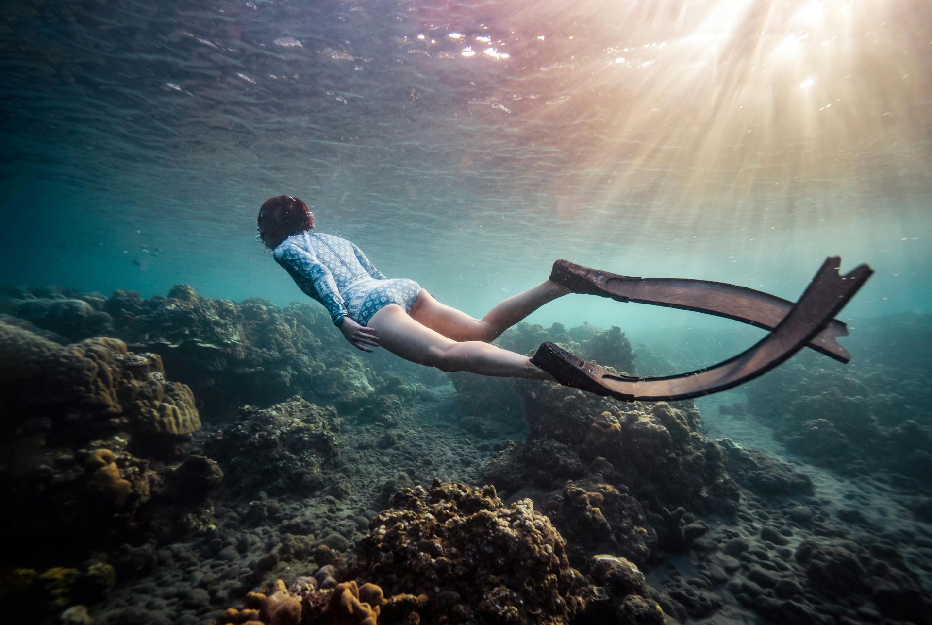 A woman is freediving in the ocean near a coral reef.