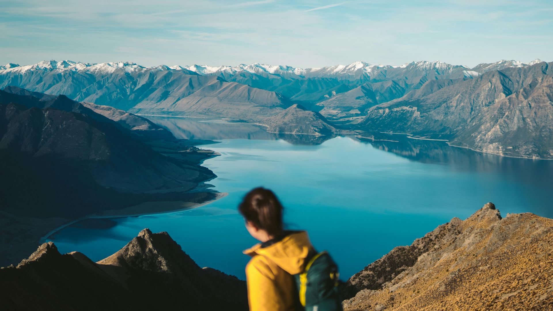 A woman is standing on top of a mountain overlooking a lake.
