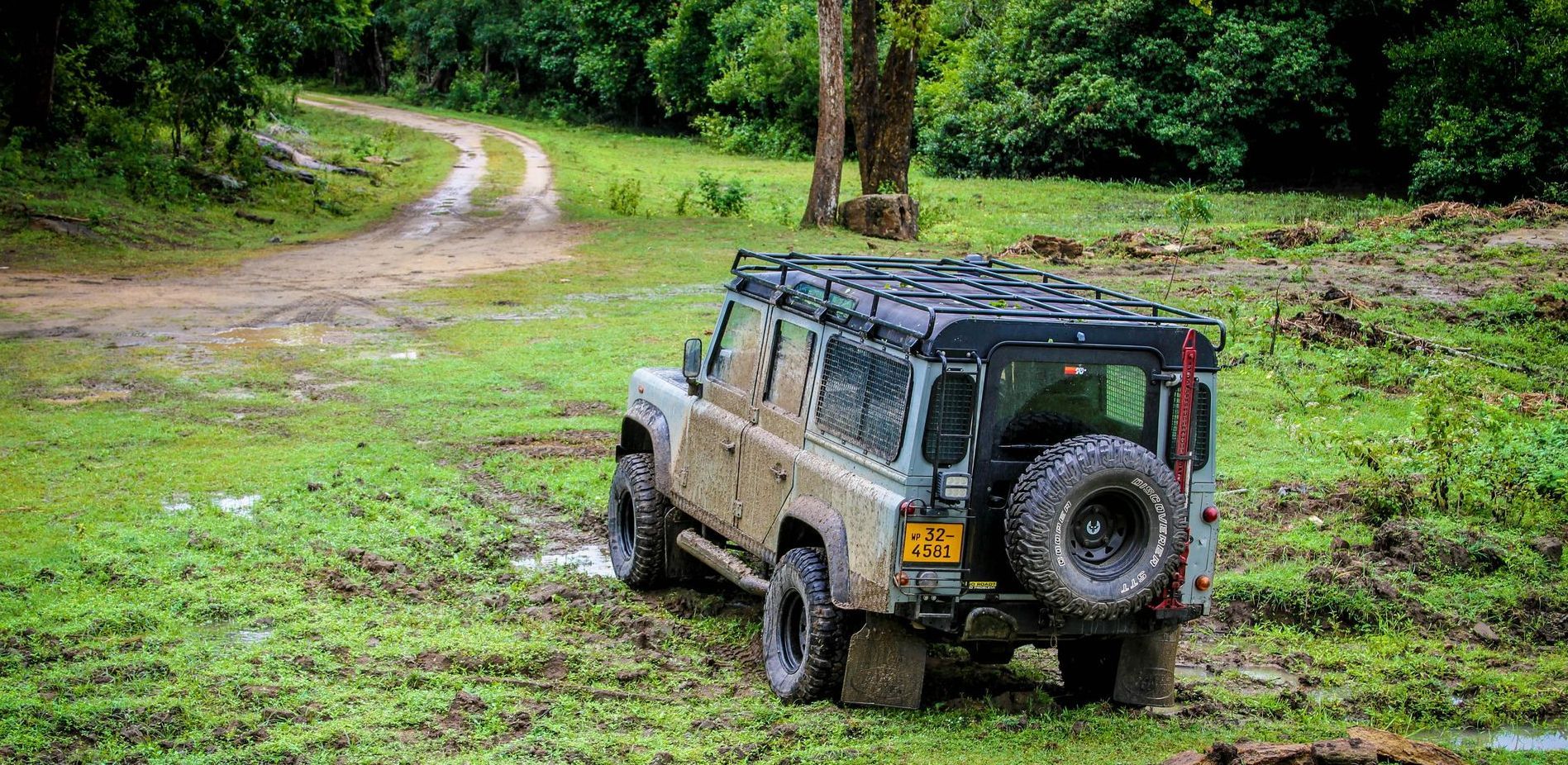 A muddy jeep is parked on the side of a dirt road in a national park in Sri Lanka