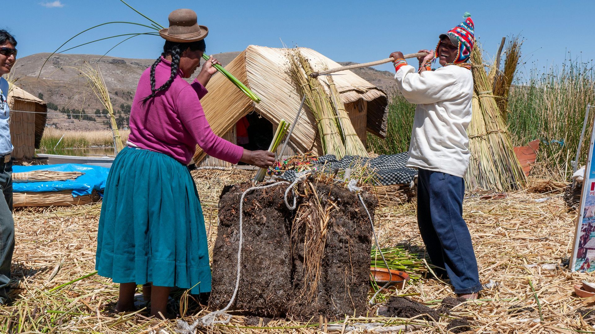 Uros Cutlure, a man and a woman withinare standing in a field with a thatched hut in the background.