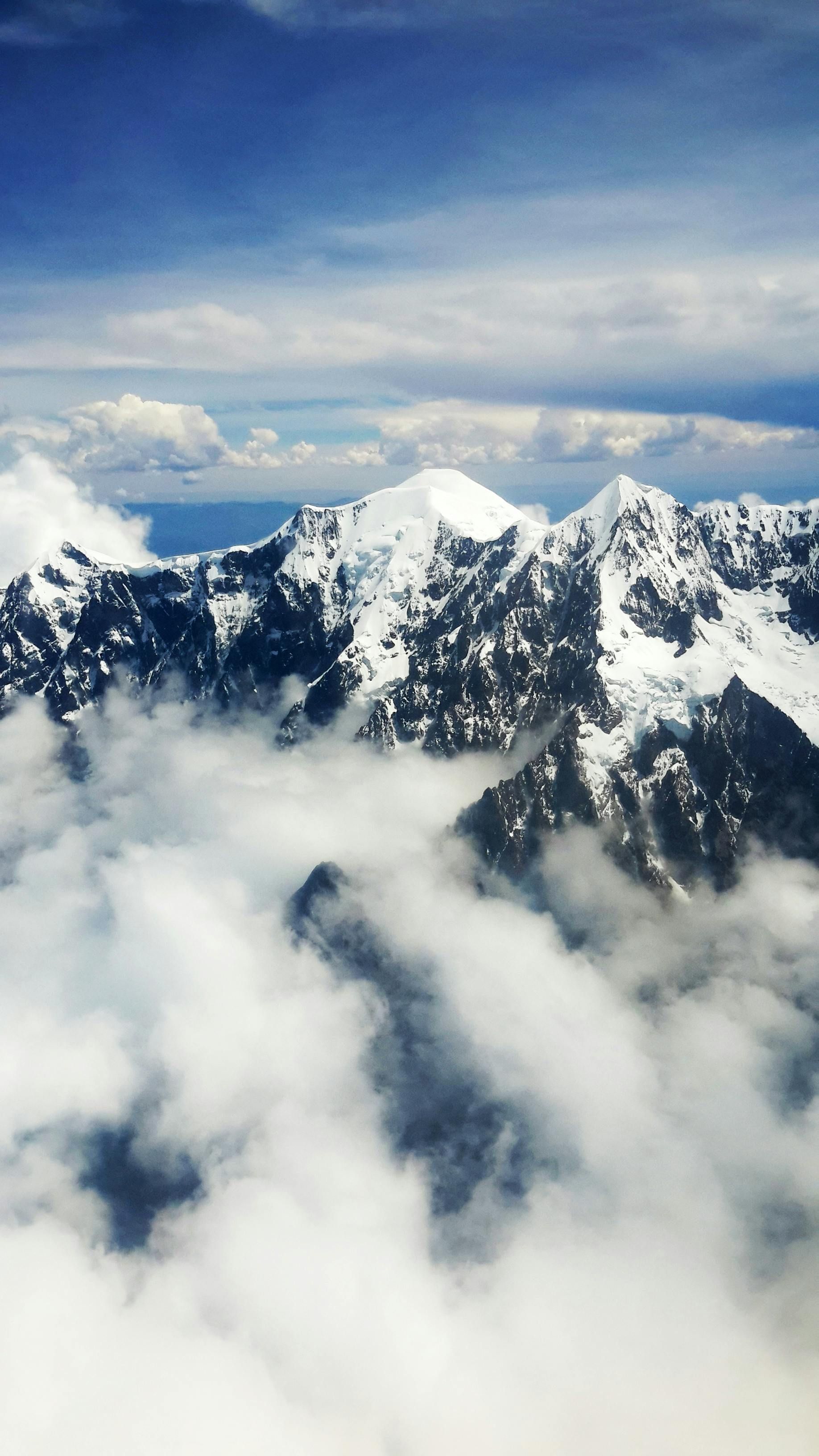 An aerial view of a snowy mountain range surrounded by clouds in Bolivia Andes