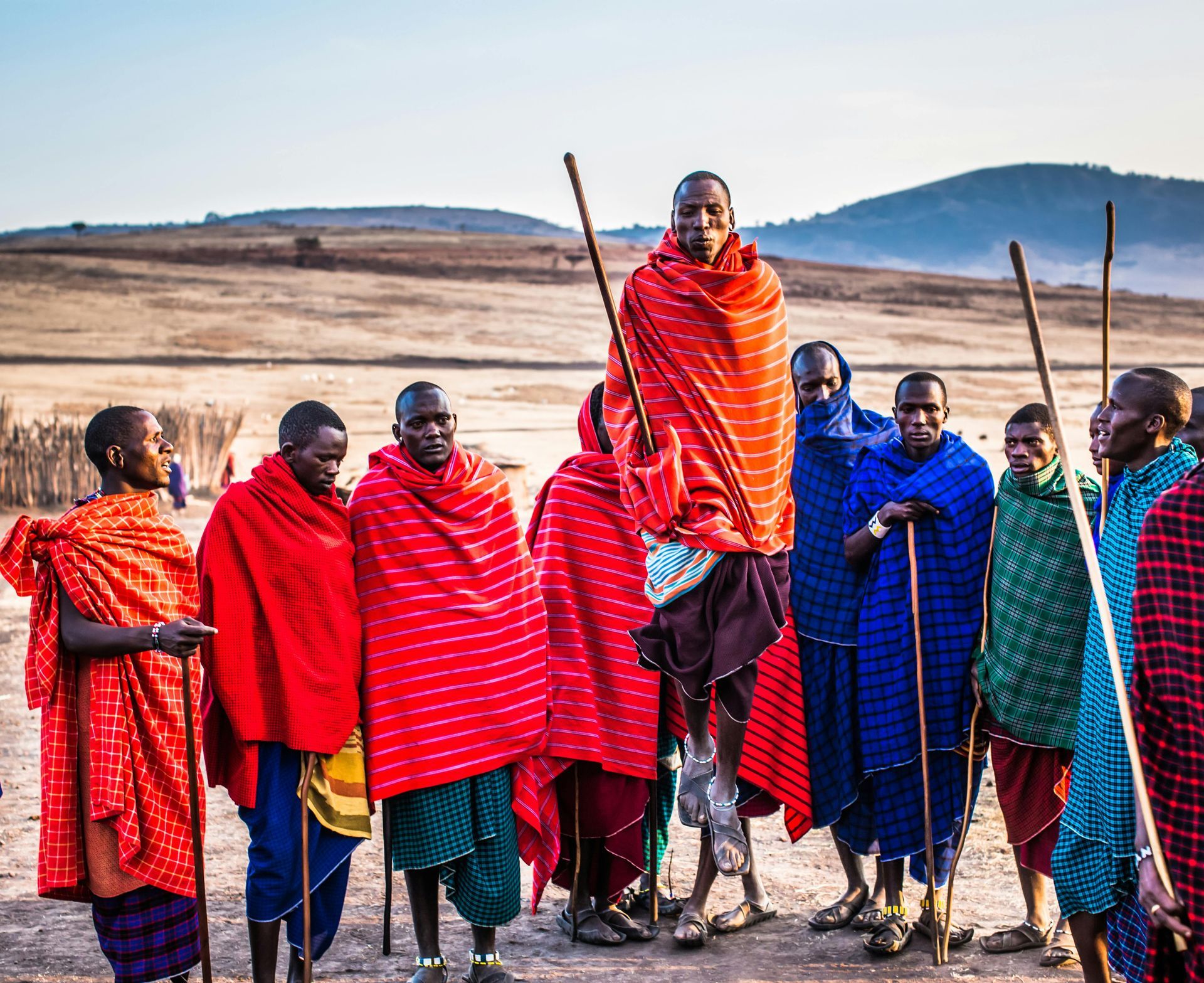 A group of Masai people are standing in a field holding sticks.