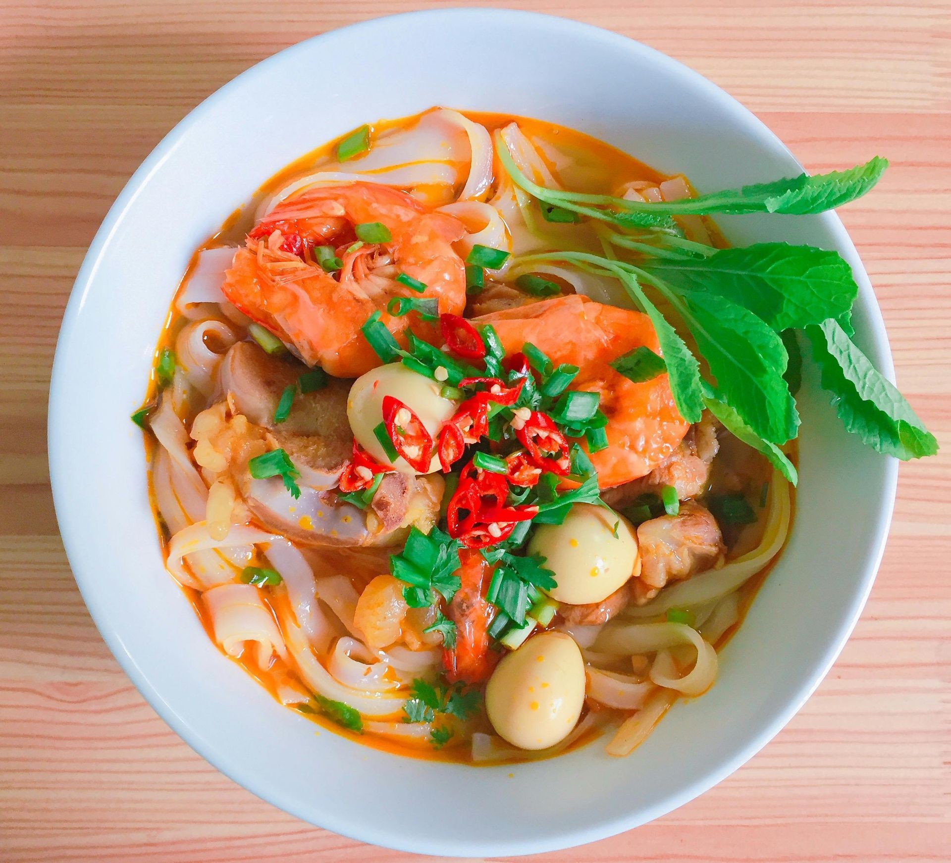 A bowl of soup with noodles and shrimp on a wooden table called Pho.