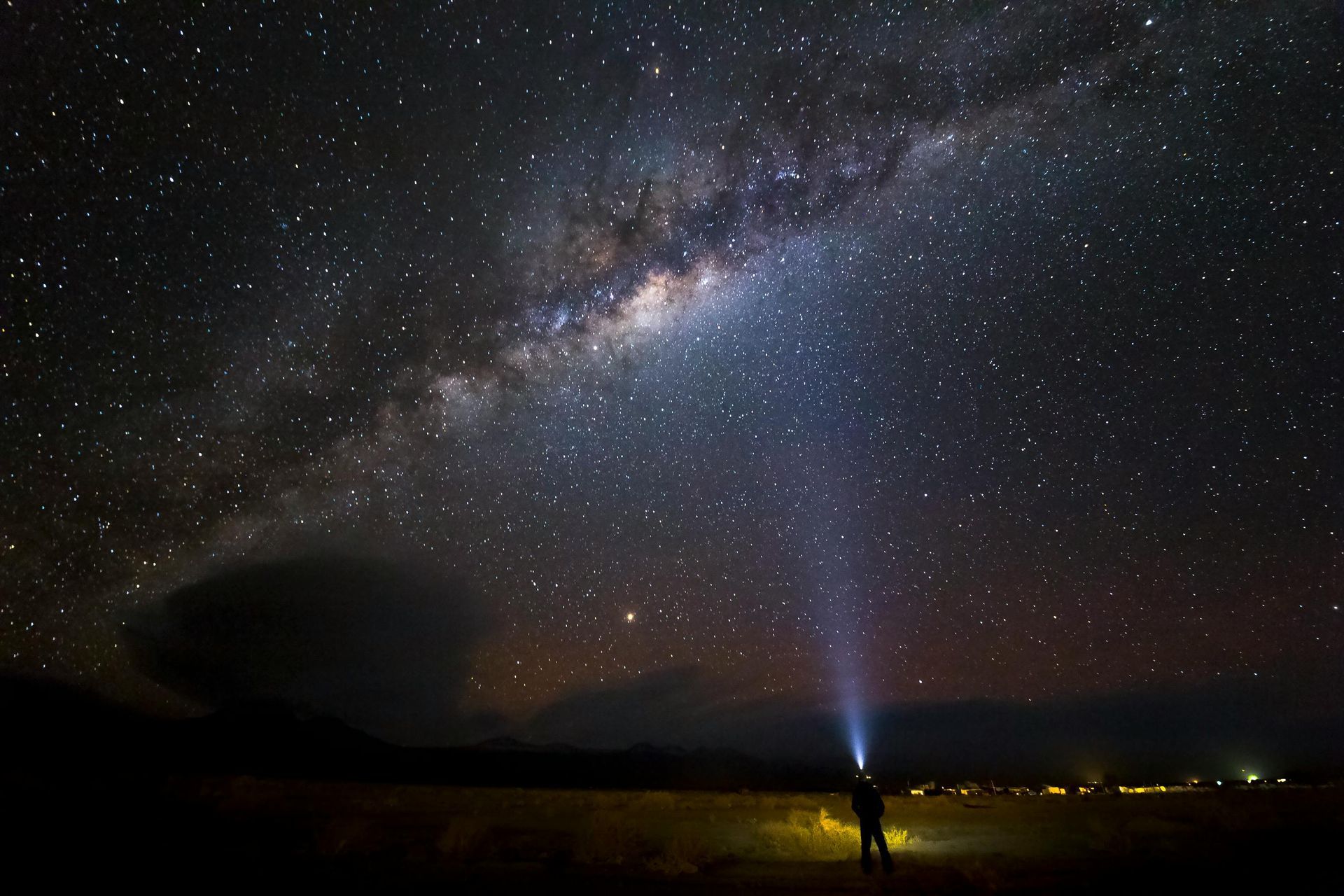 A person is standing under a starry night sky with a flashlight in their hand in the Atacama Desert