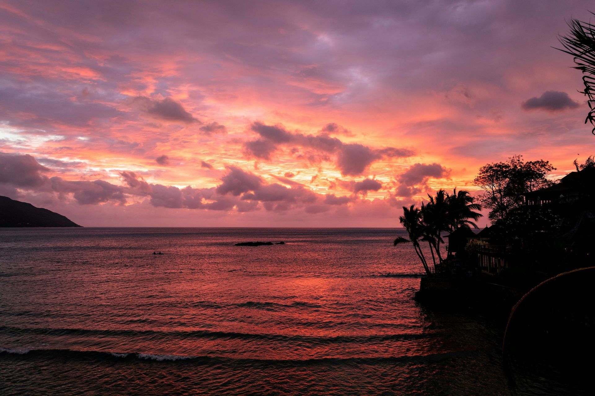A sunset over a body of water with palm trees in the foreground in Seychelles