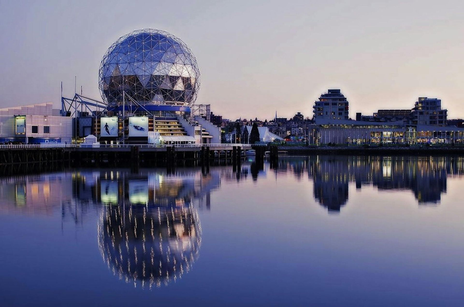 The Science World building in Vancouver, a geodesic dome structure, reflected in calm water at dusk.