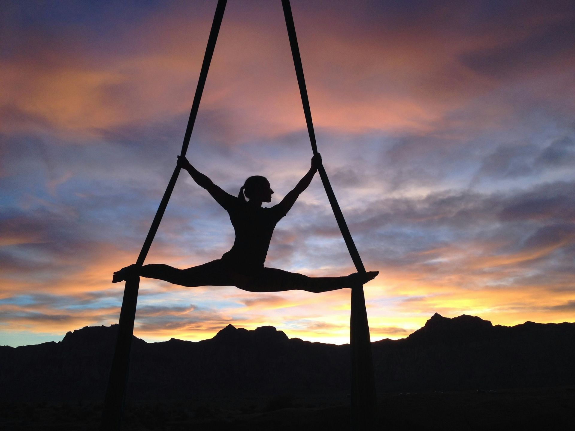 A silhouette of a woman doing aerial acrobatics at sunset