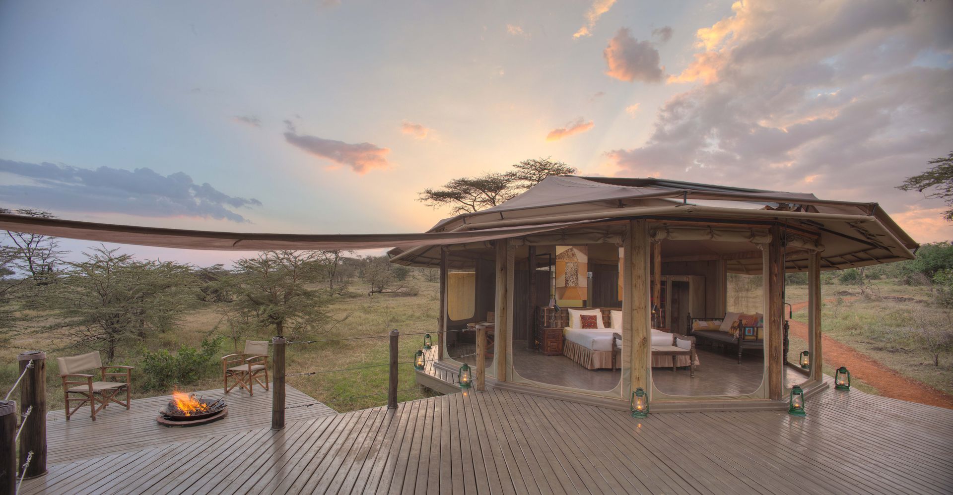 A safari tent with a deck and a fire pit in front of it at sunrise at Leopard Hill