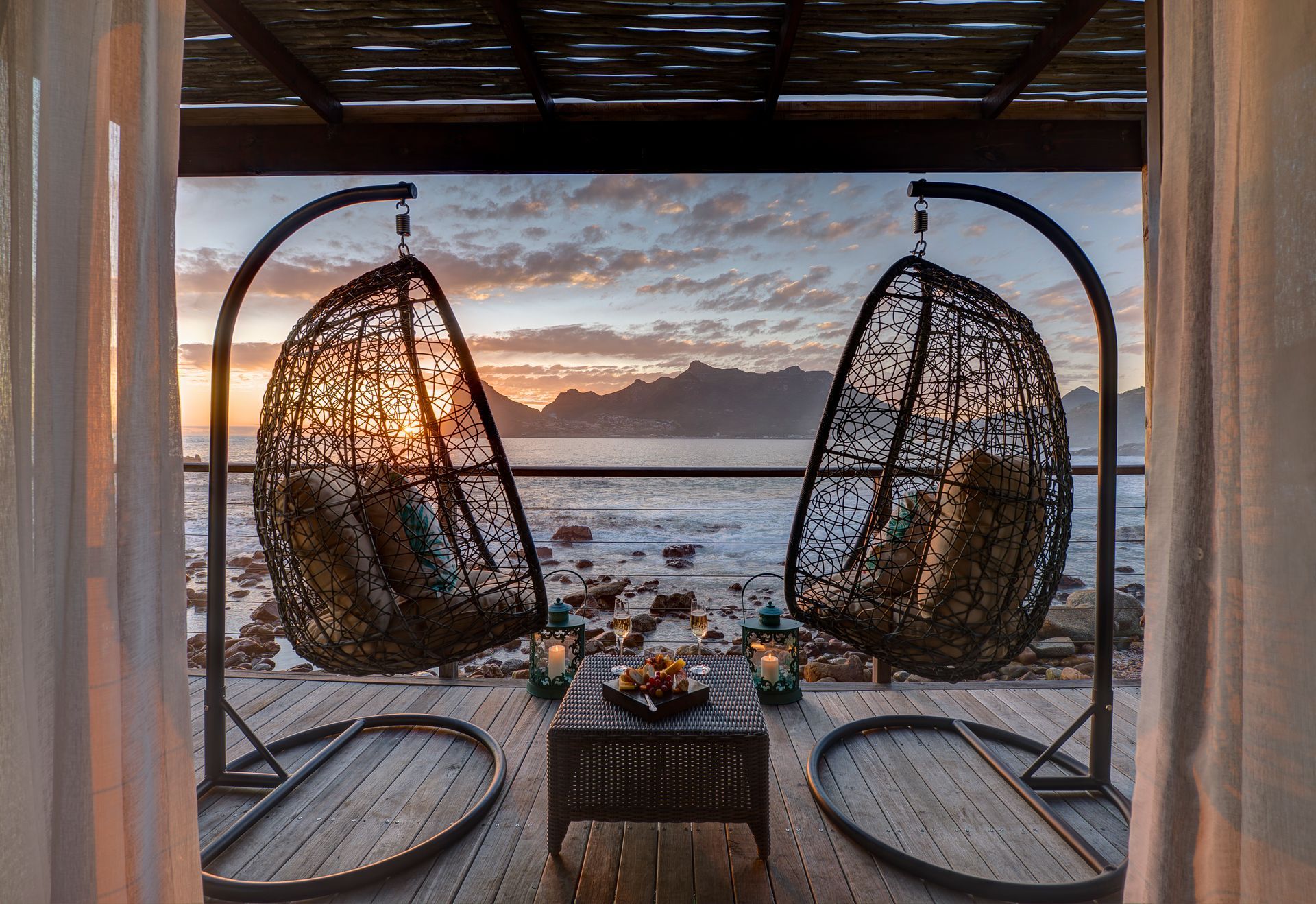 Two hanging chairs are sitting on a wooden deck overlooking the ocean at Tintswalo Atlantic
