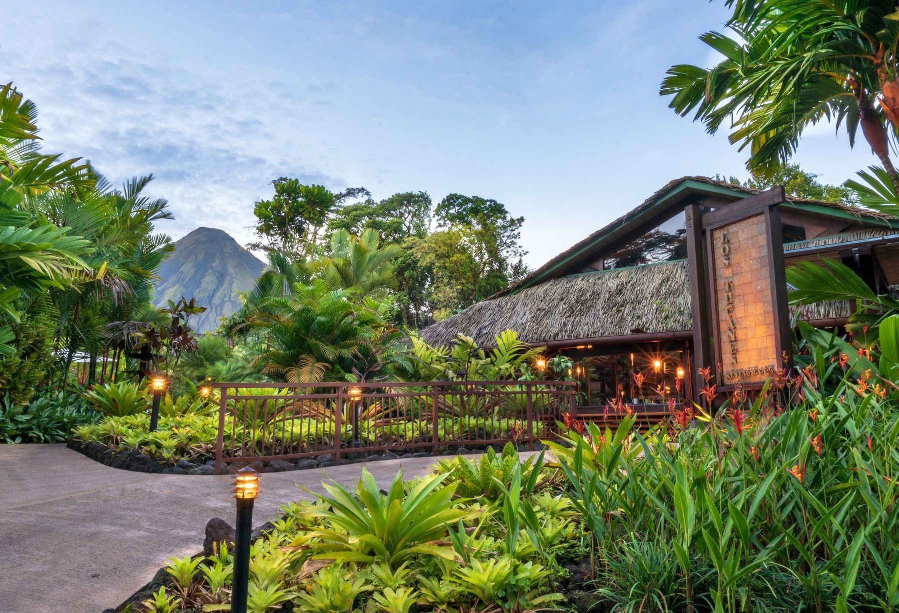 A house with a thatched roof is surrounded by trees and bushes with Volcano.