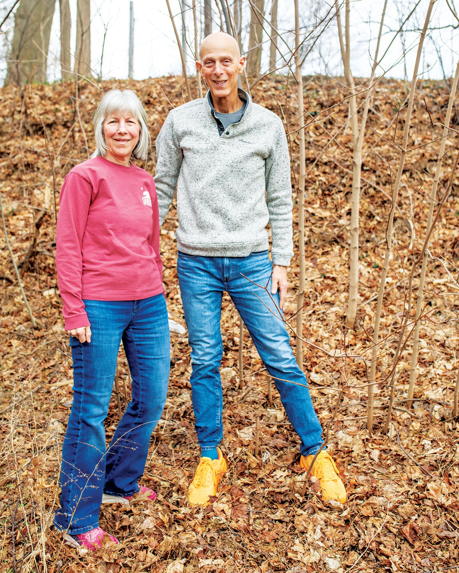 A stack of books sits on a wooden table, next to a lit candle and a warm cup of coffee or tea.