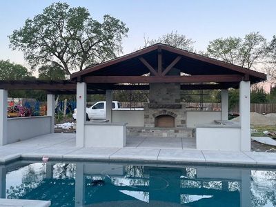 A patio with a fireplace and a pool in the background