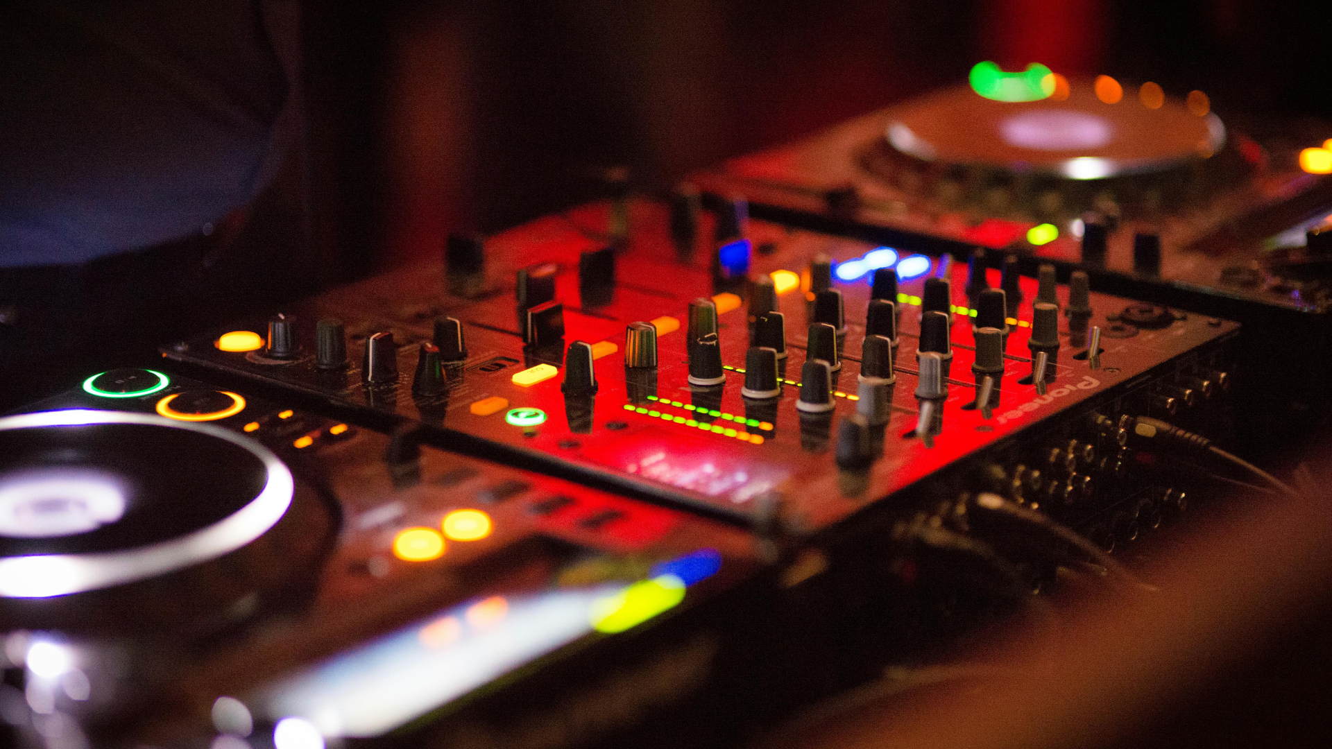 DJ equipment with illuminated knobs and buttons in vibrant red, blue, and green lights at a live event.