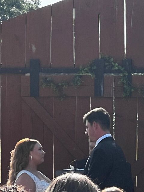 Event pricing for DJ services at K & D Disc Jockey & Karaoke. Couple exchanging vows at an outdoor wedding ceremony, standing in front of a wooden fence with greenery surrounding them.