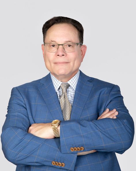 A man in a blue suit and tie is standing with his arms crossed.