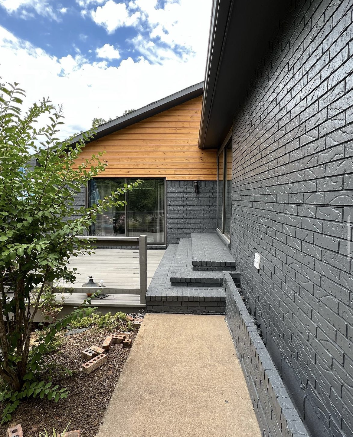 a black brick house with a wooden siding and a walkway leading to it .