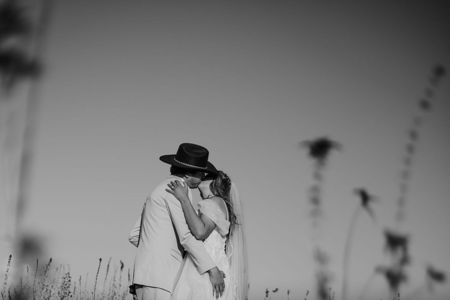 A black and white photo of a bride and groom hugging in a field.