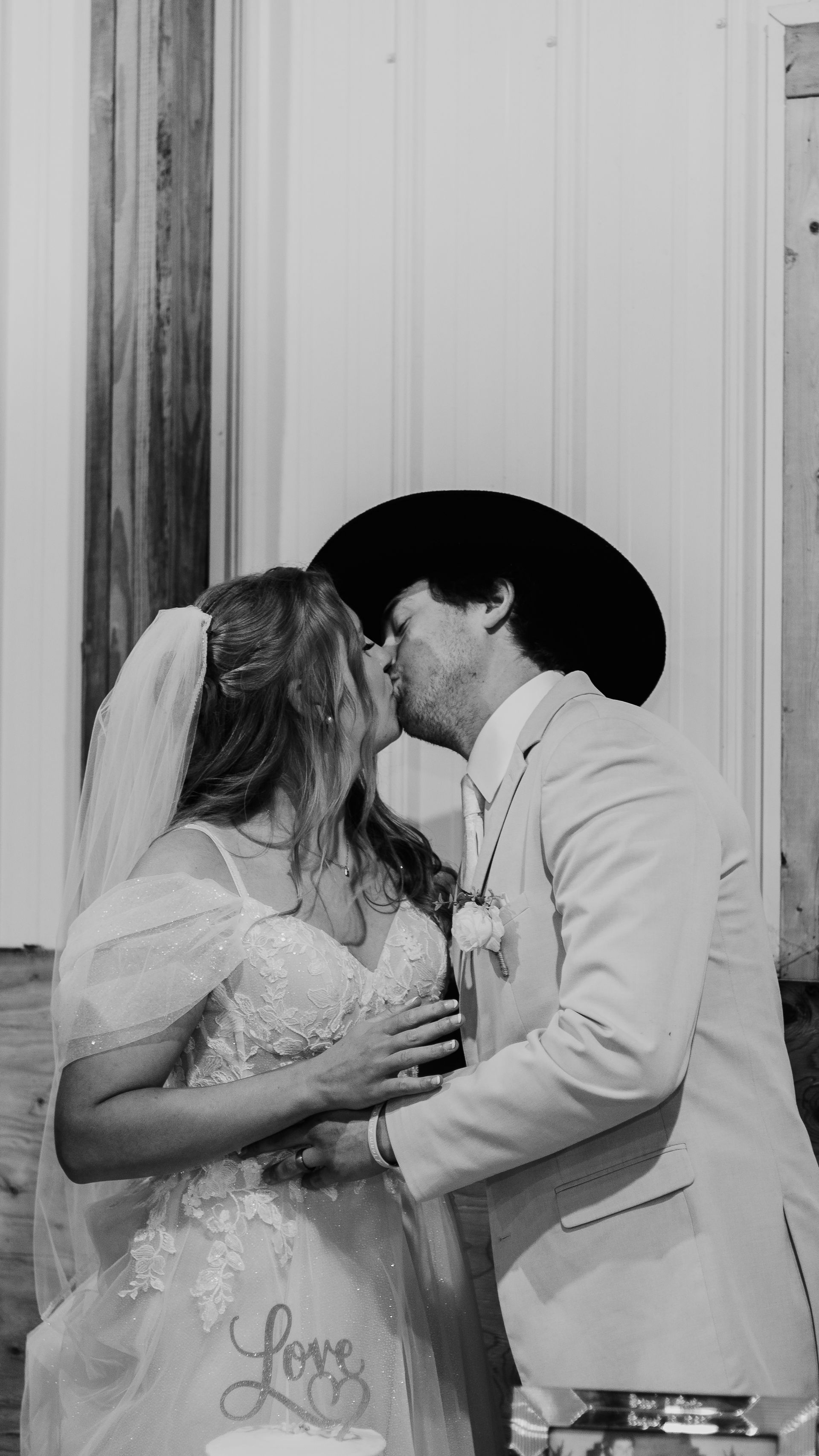A black and white photo of a bride and groom kissing at their wedding.