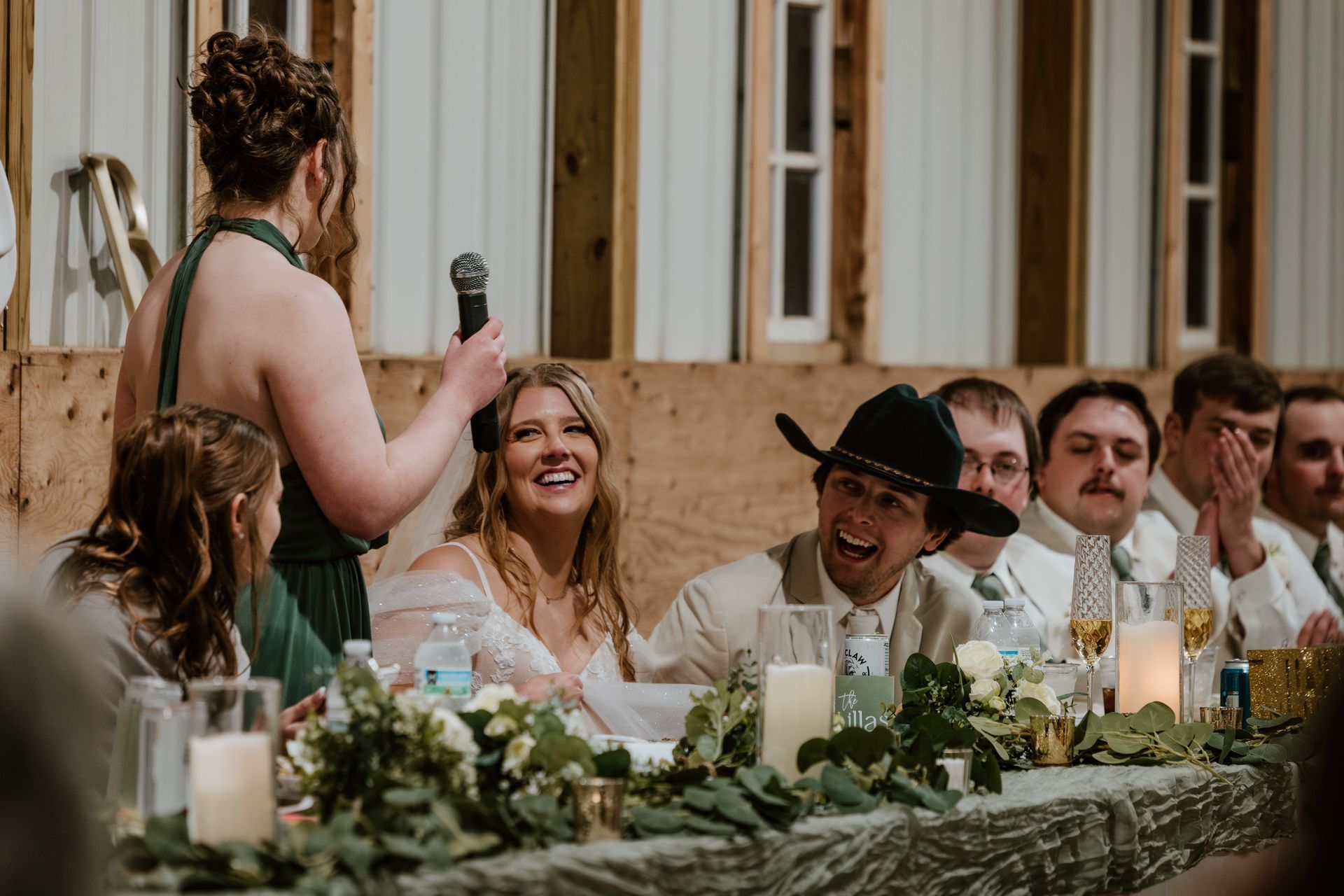 A woman is holding a microphone in front of a group of people at a wedding reception.
