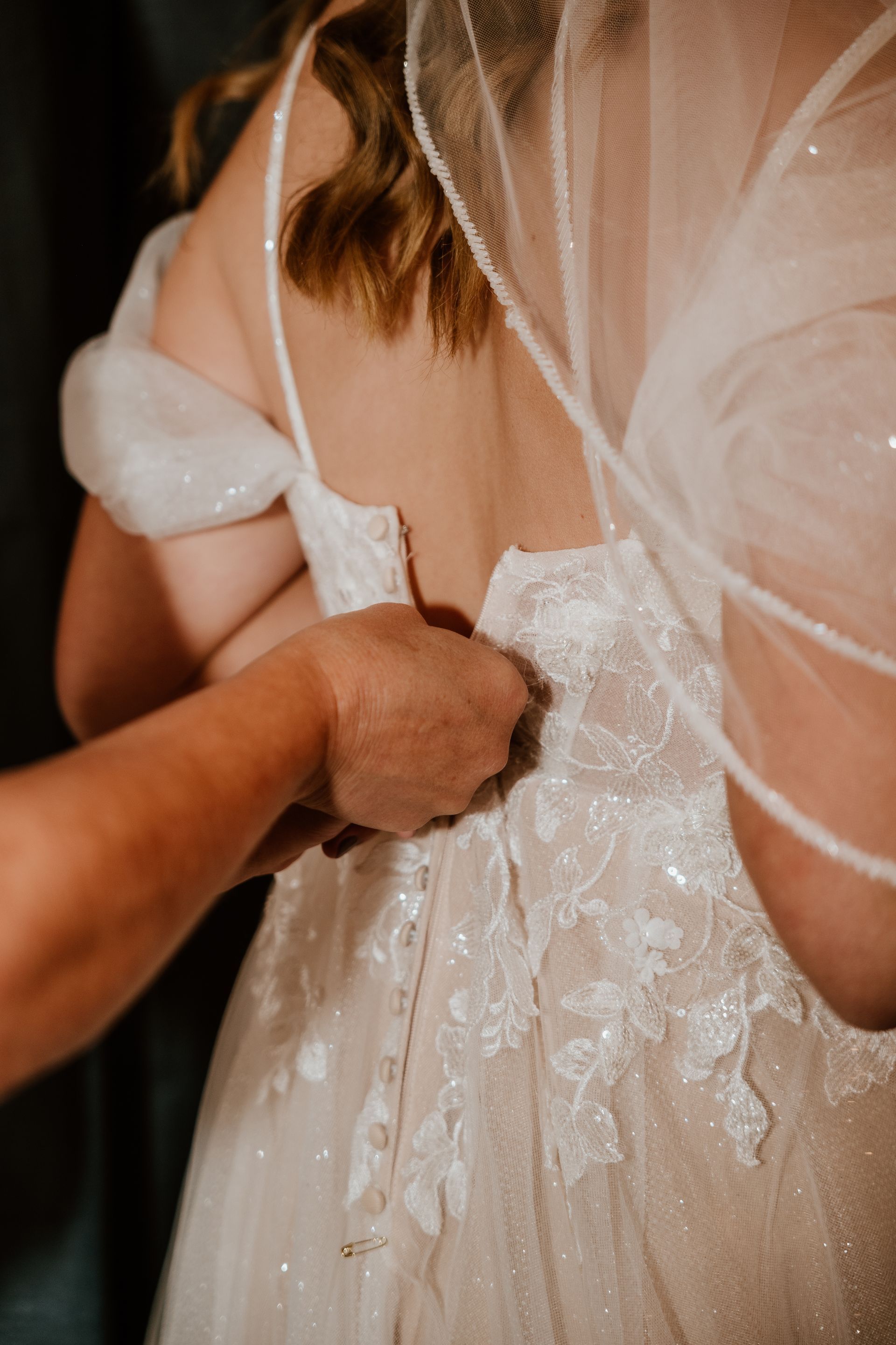 A woman is helping a bride put on her wedding dress.