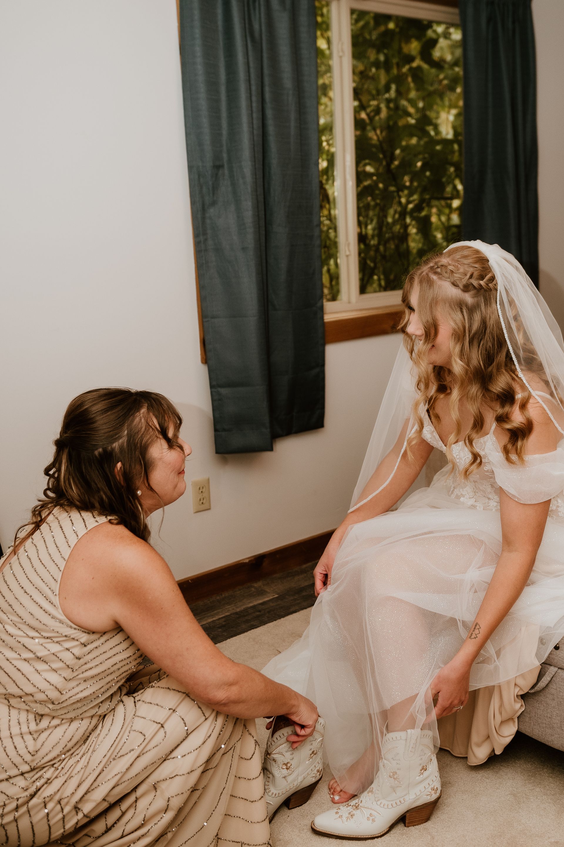 A woman is helping a bride put on her wedding boots.