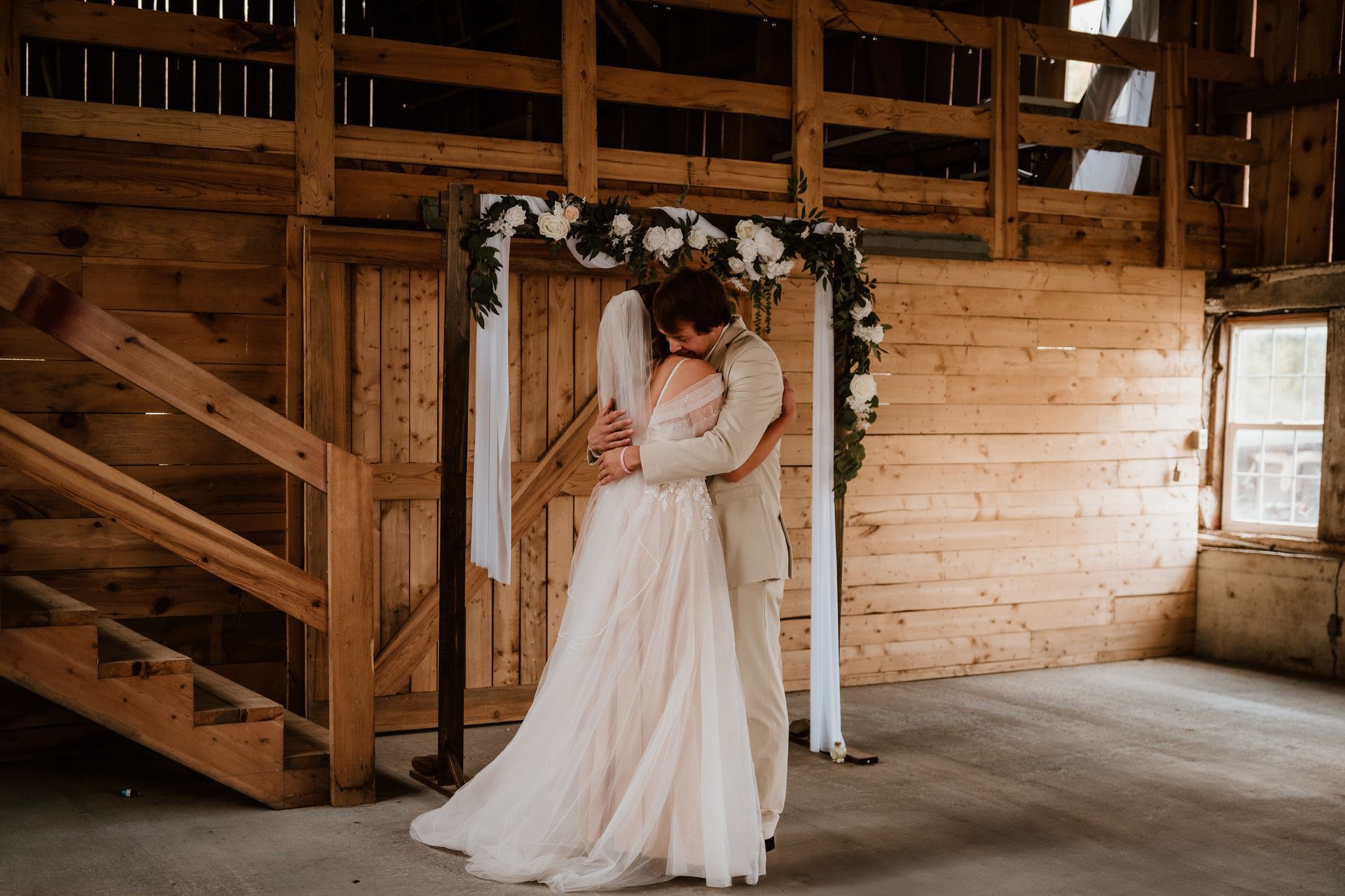 A bride and groom are hugging each other in a barn.