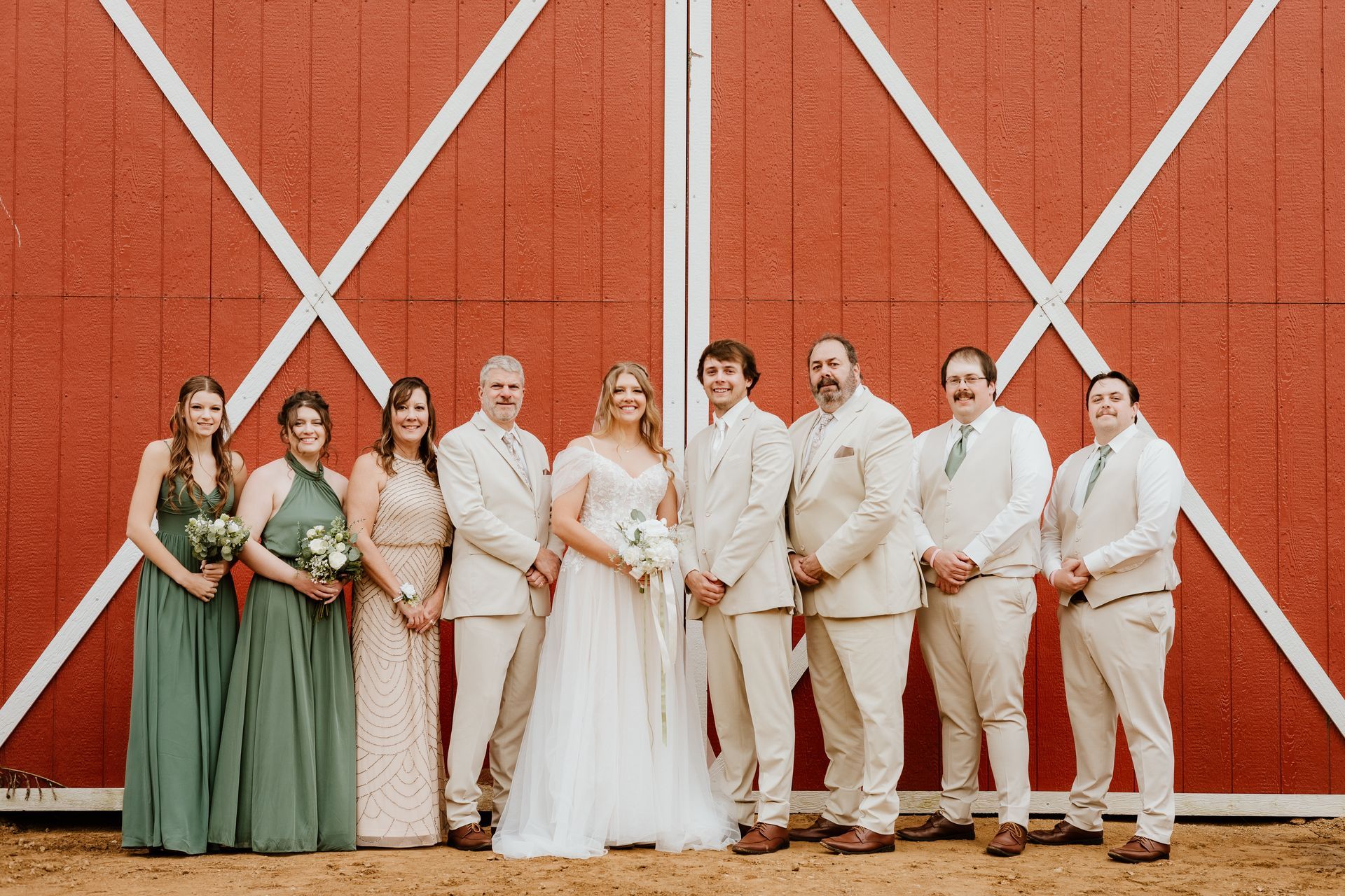 The bride and groom are posing for a picture with their wedding party in front of a red barn.