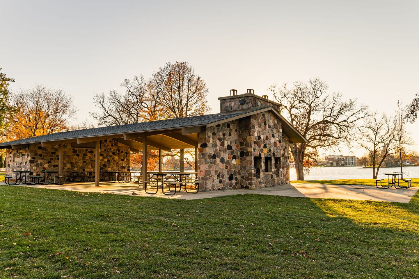 A stone pavilion with tables and benches in a park.